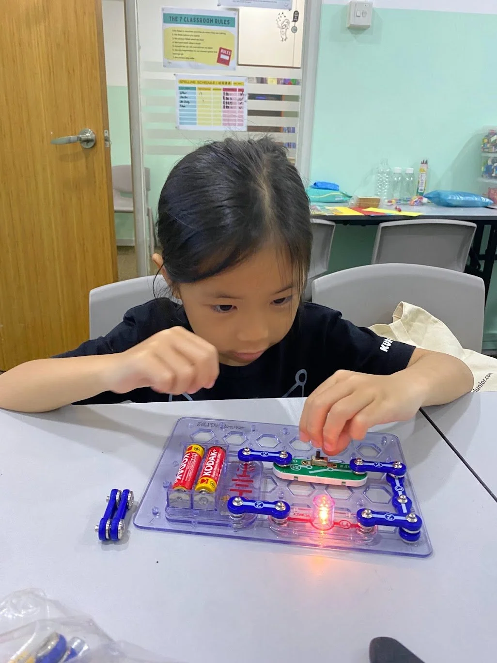 Child building a working electrical circuit with a hands-on STEM kit, lighting up an LED
