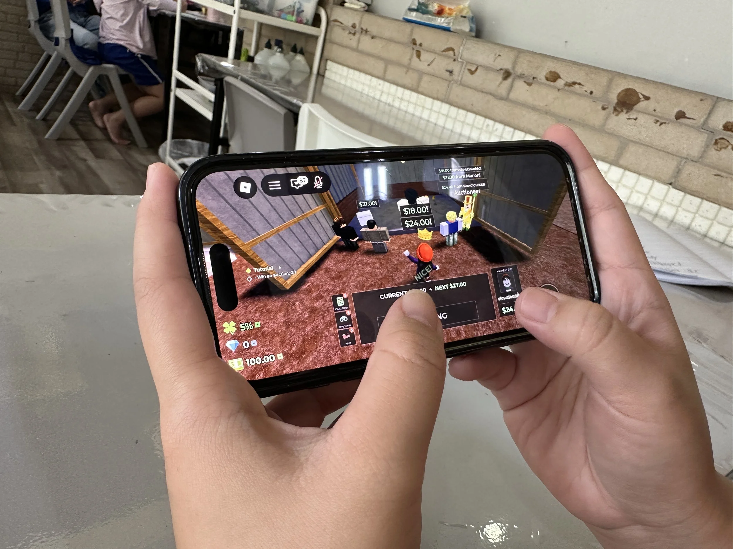 Close-up of a child's hands playing a Roblox auction mini-game on a smartphone