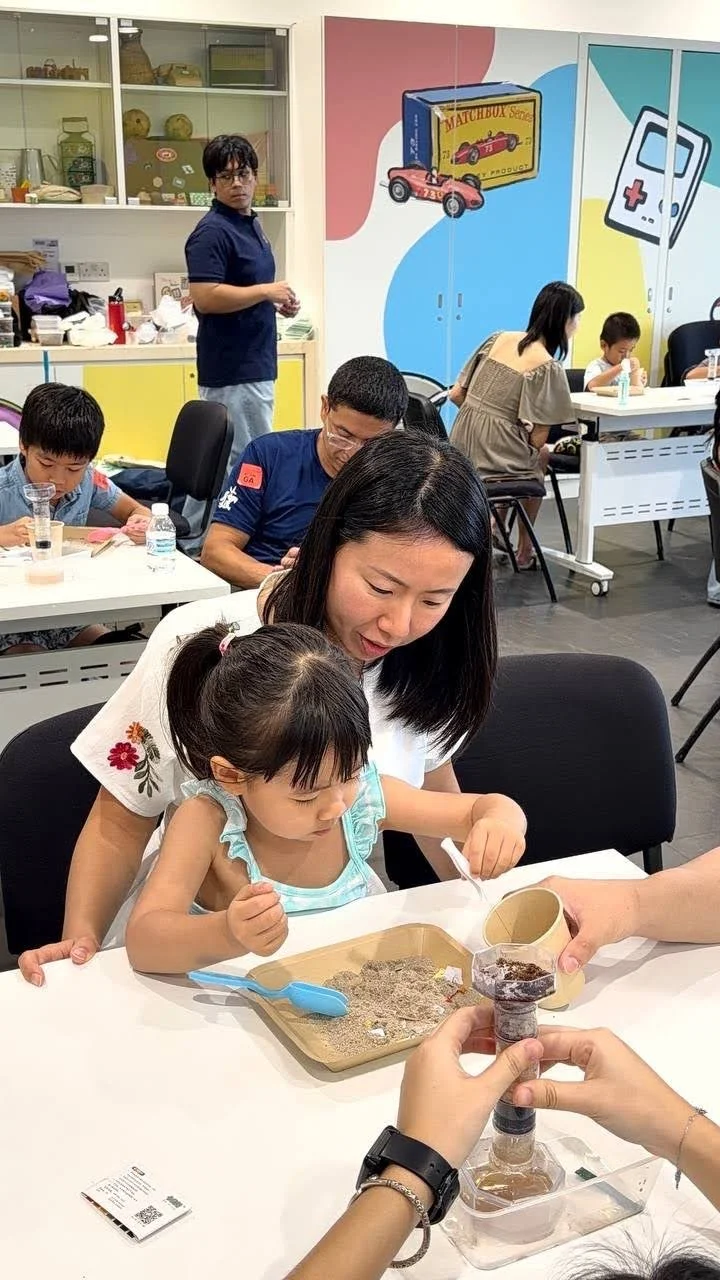 A woman and a young girl are interacting with a sensory activity at a table, with people and colorful murals in the background.