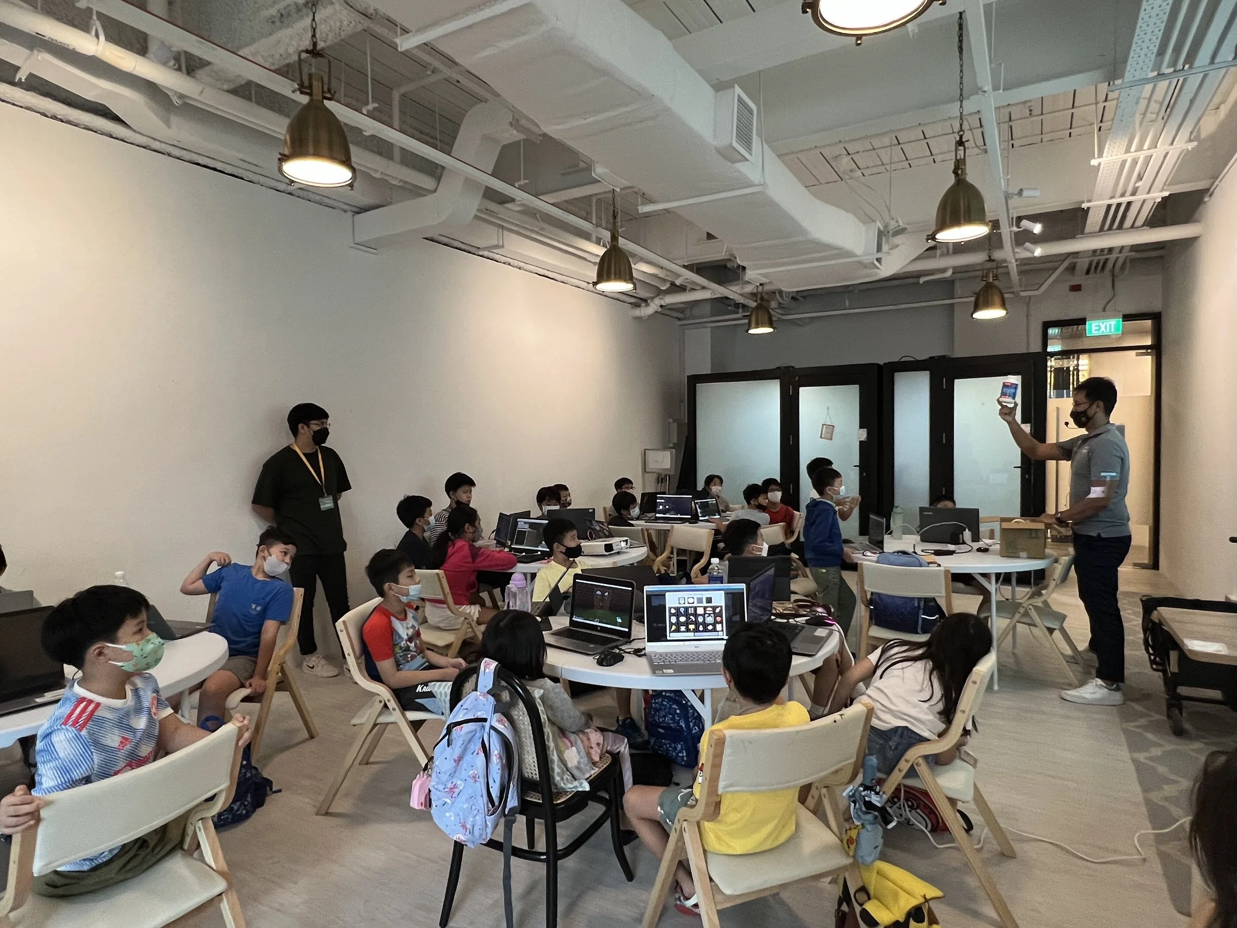 Instructor guiding a class of children through a digital literacy lesson using laptops in a Minecraft-based learning environment