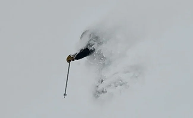 A skier in black gear making a turn in fresh powder snow.
