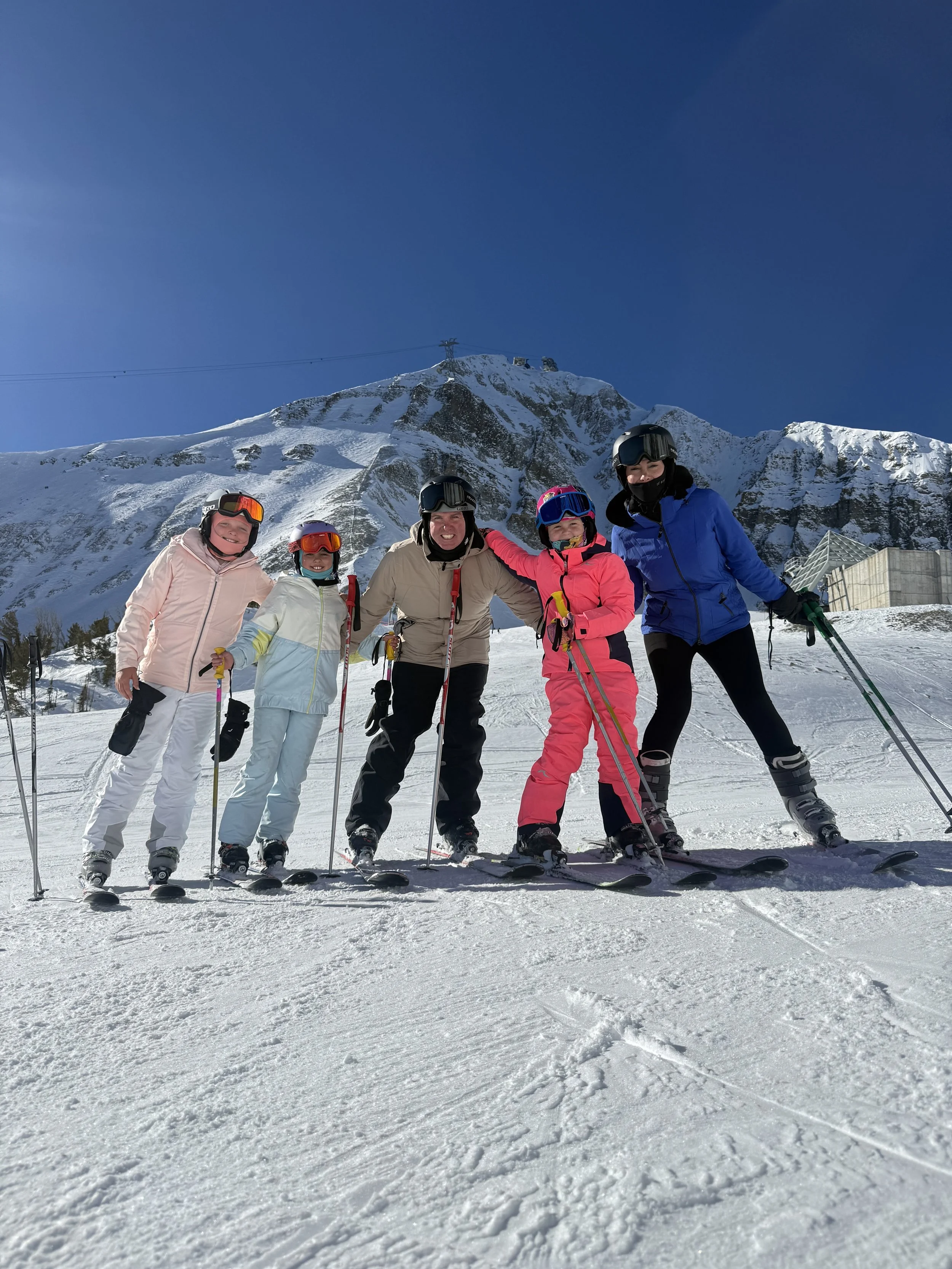 Group of five people skiing on snow-covered mountain with a clear blue sky and mountain in the background.