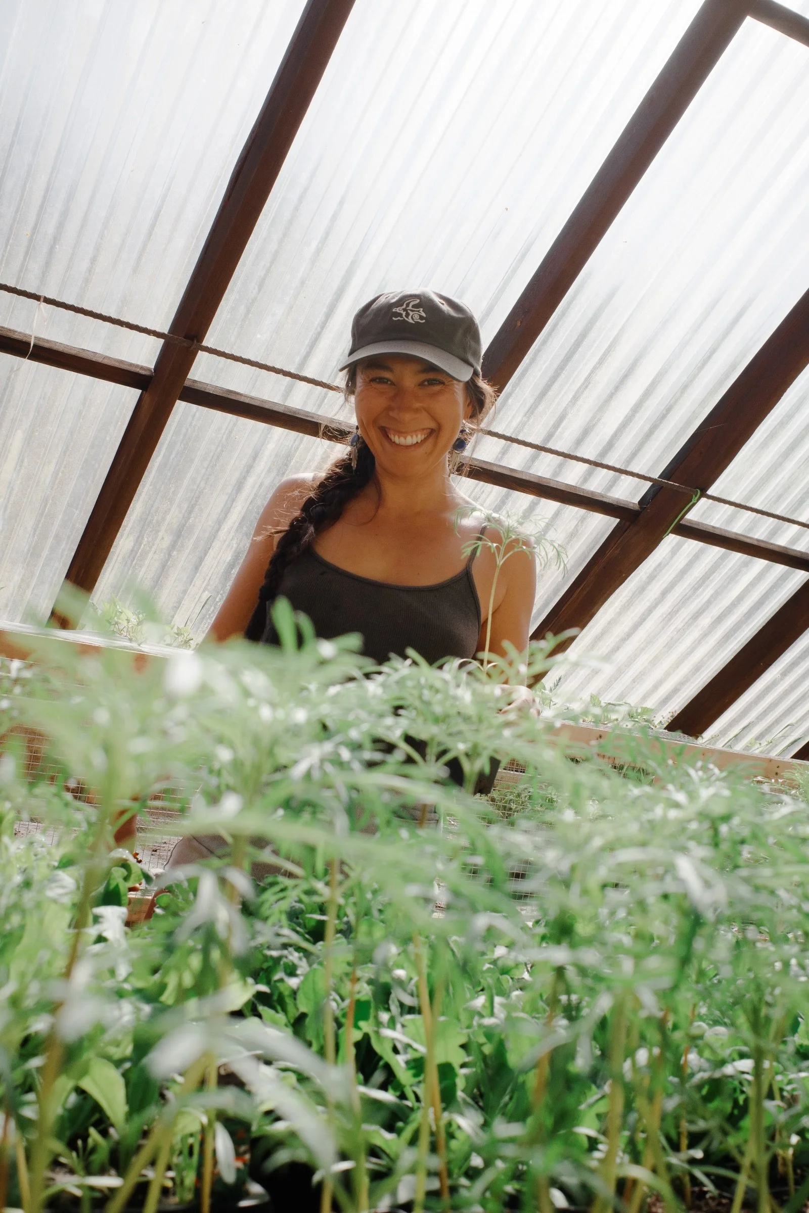 Woman smiling in a greenhouse with plant seedlings in front of her.
