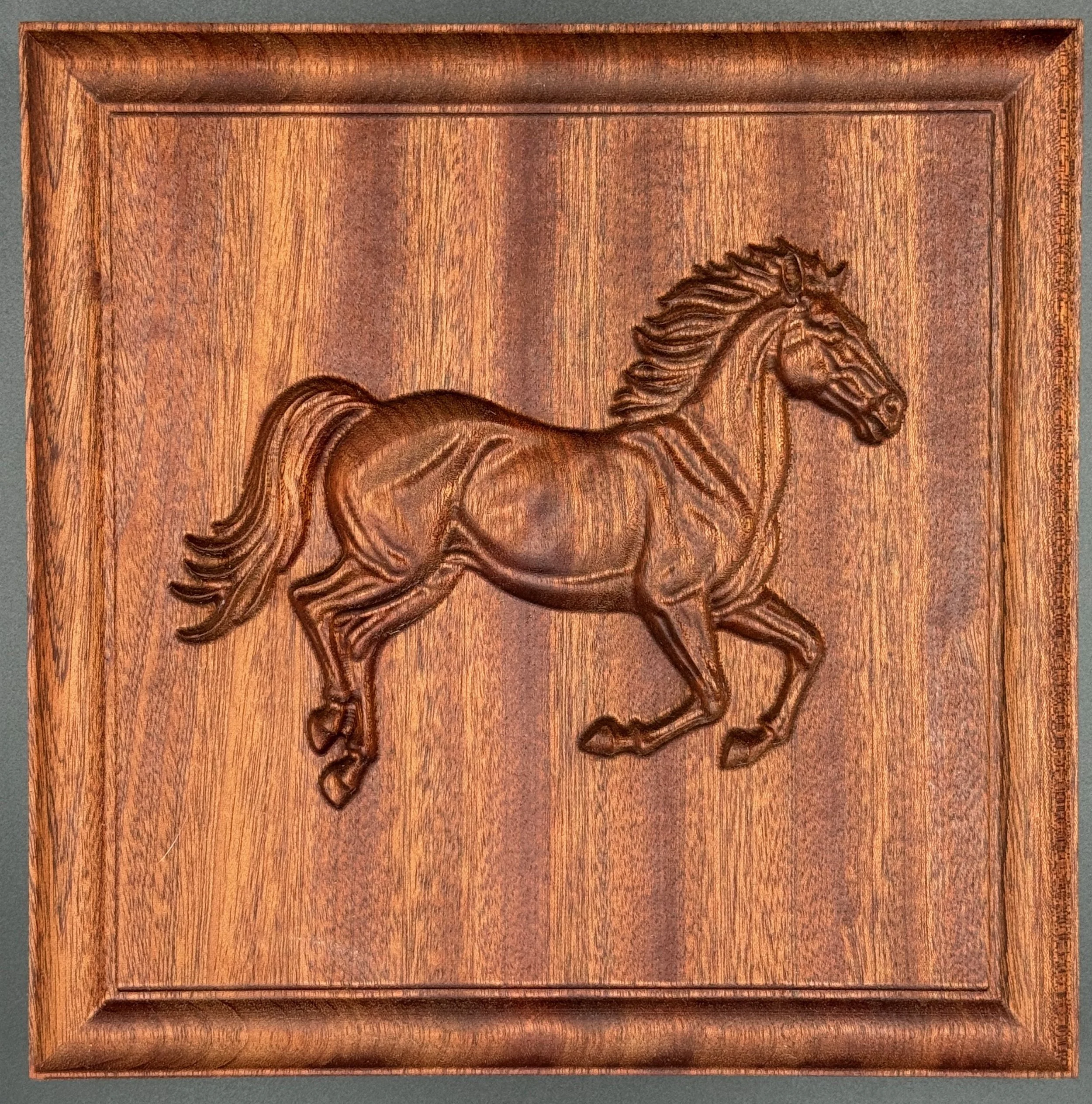 Wooden plaque with a carved relief of a running horse.