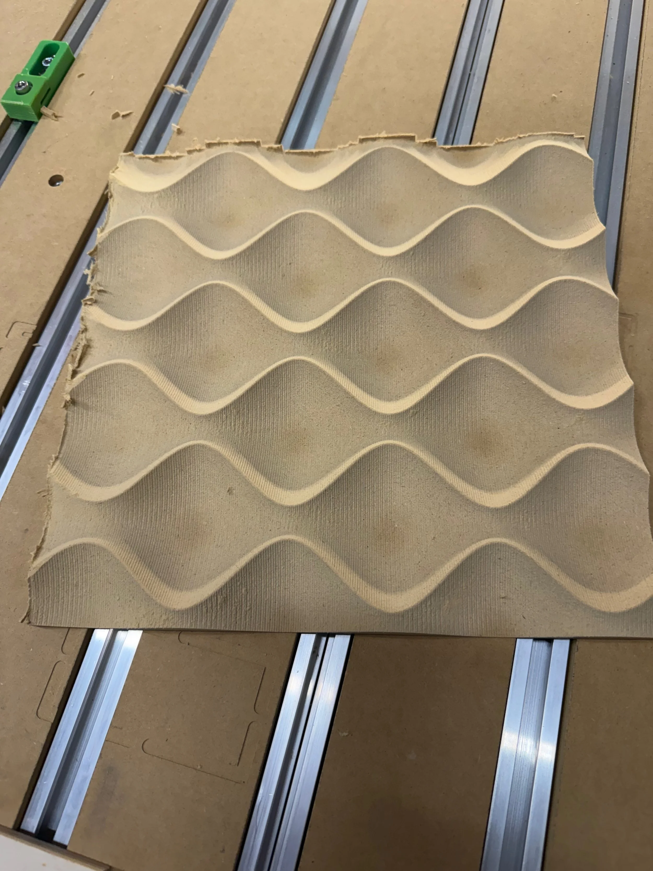 A piece of foam with a wavy pattern on a work table with metal rails.