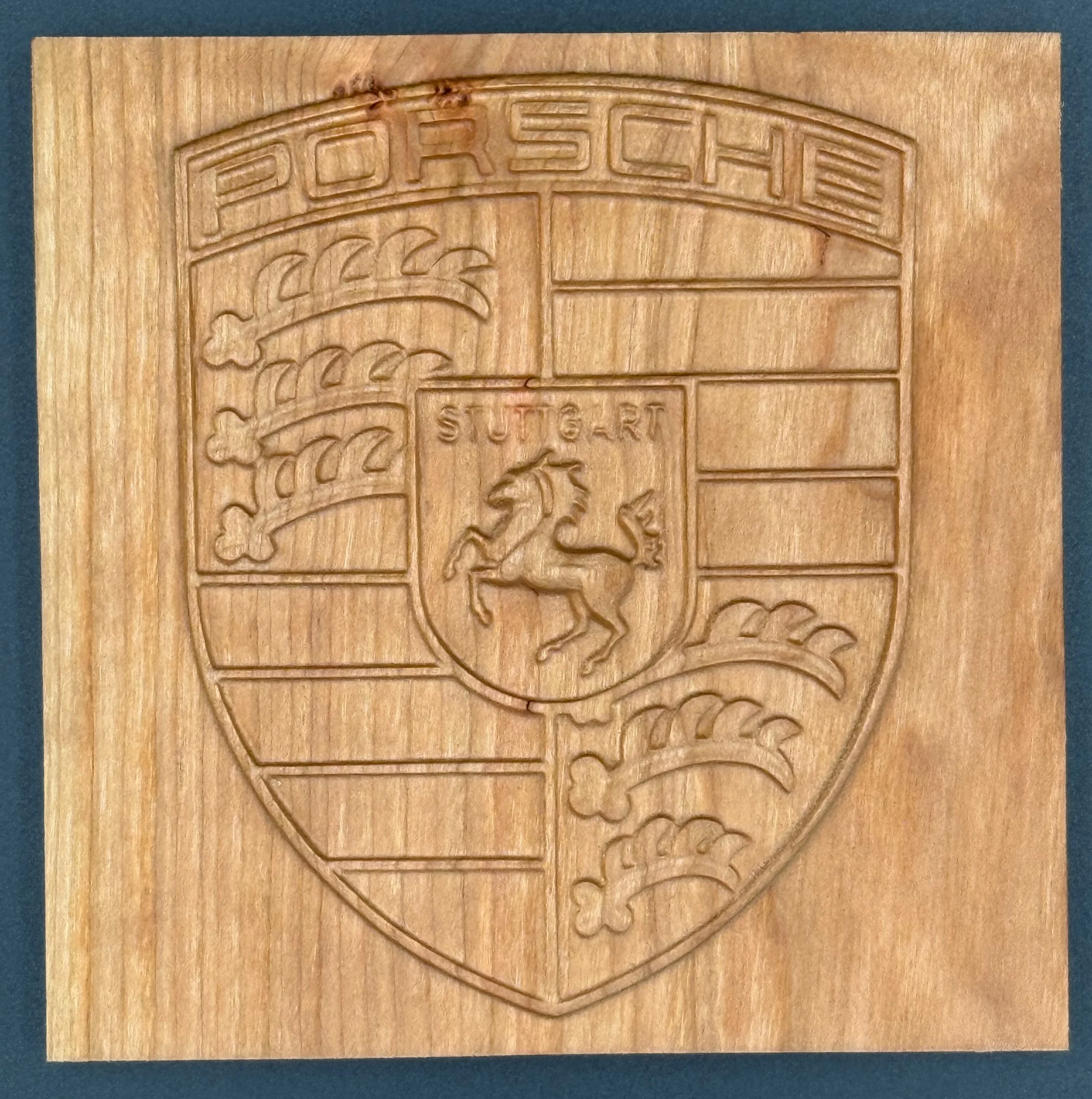 Wooden plaque engraved with the Porsche logo, featuring a lion inside a shield with the word "Stuttgart" above it, and a crest with a horse and three feathers.