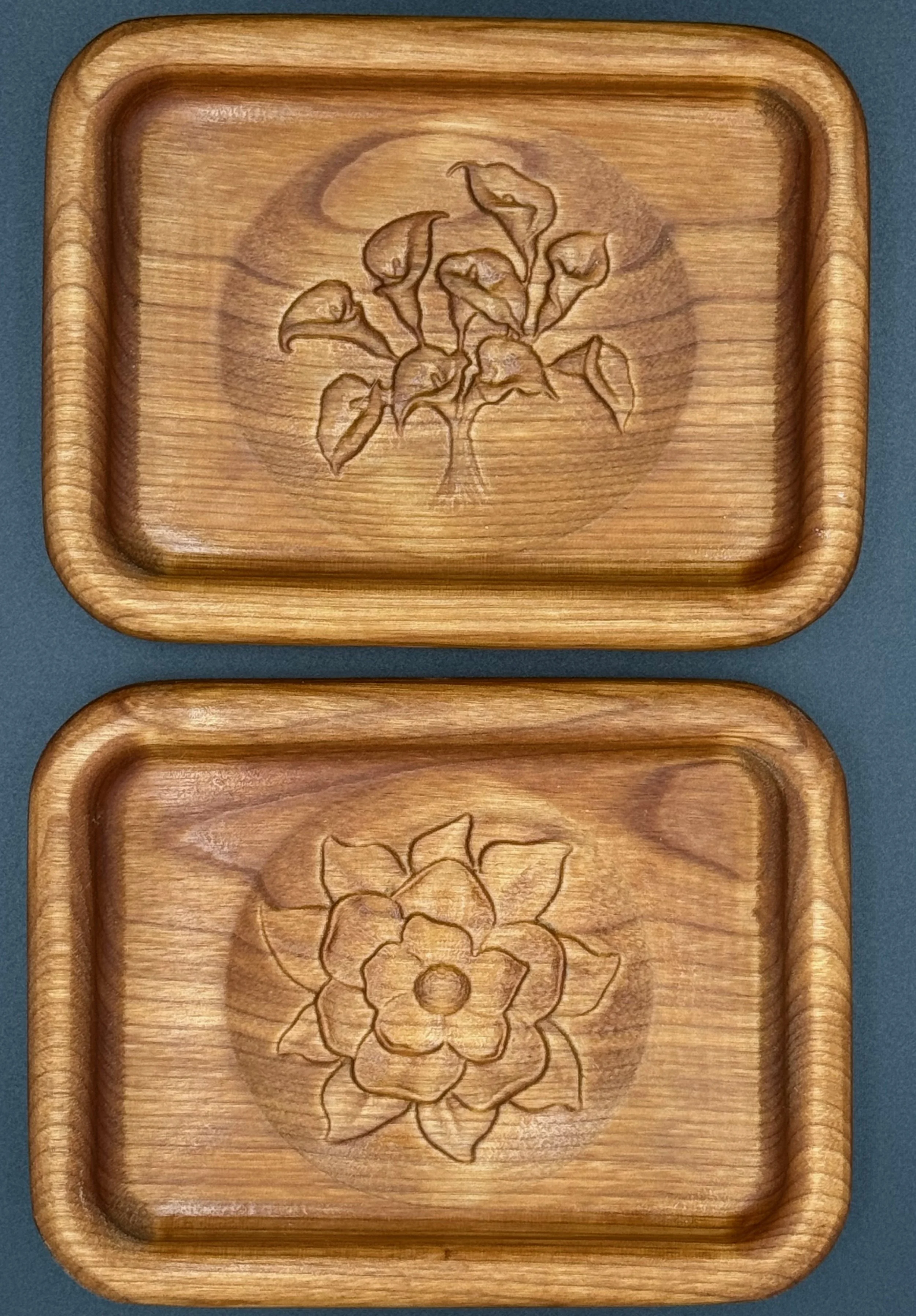 Two wooden trays with carved floral designs, placed on a dark surface.