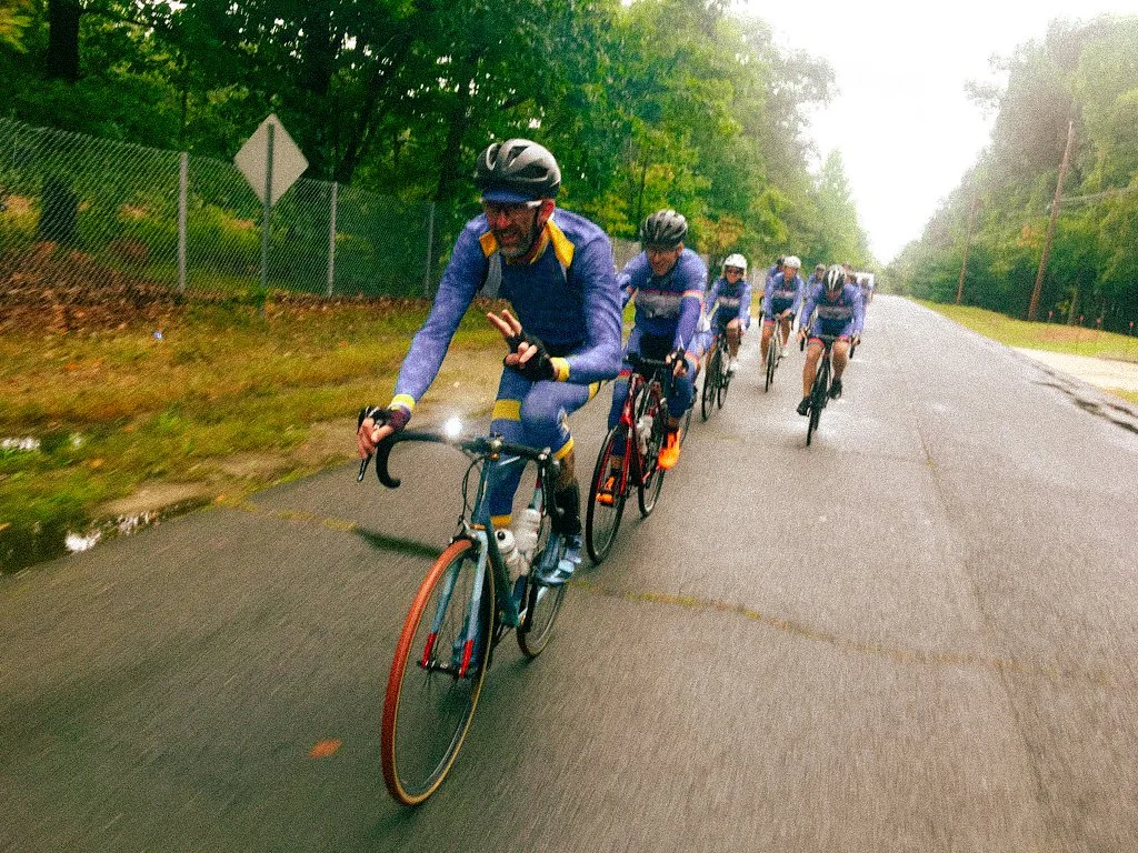 Cycling coach Woody leading a group of riders on a road in the woods.