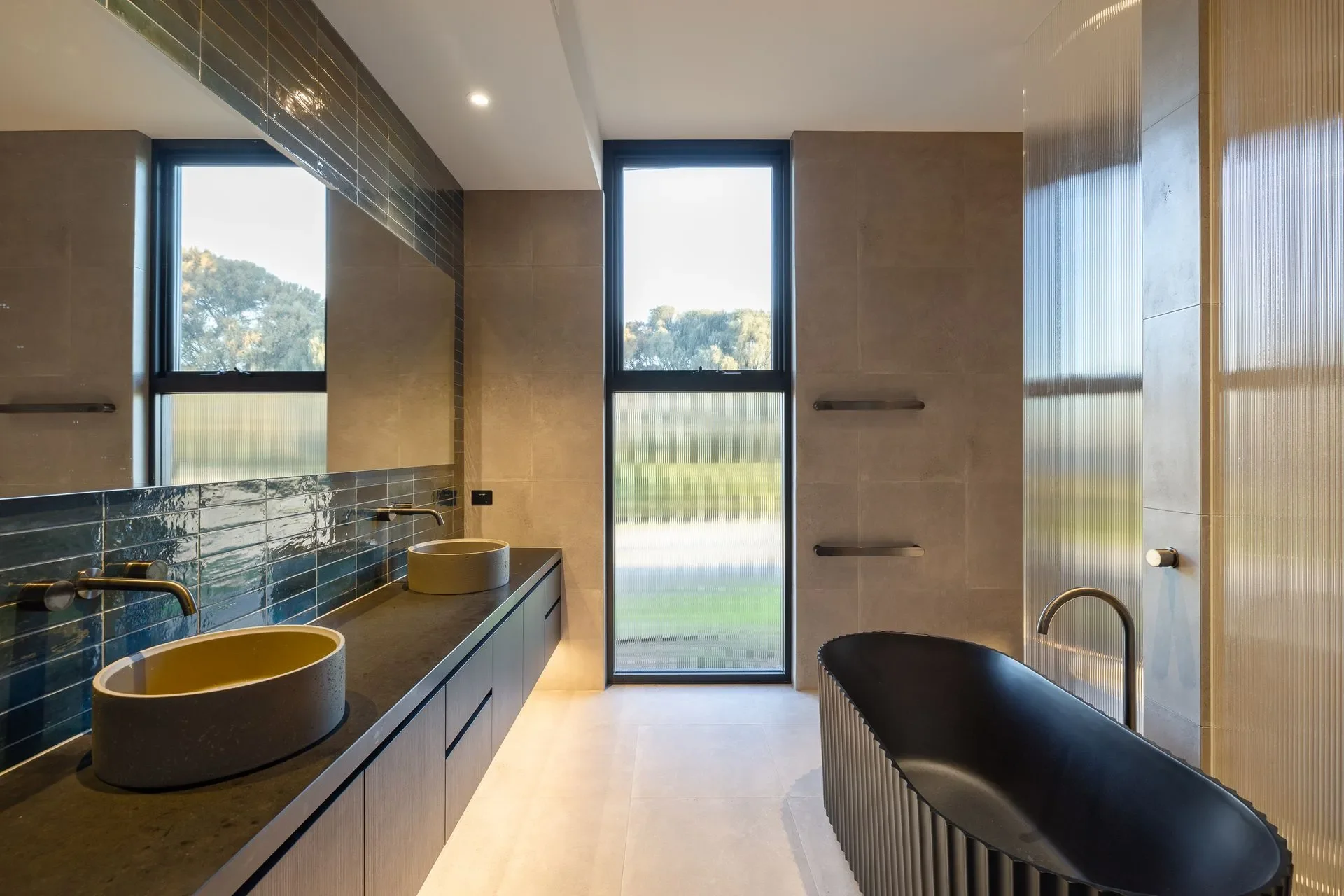 Double bathroom sinks with turquoise tiling. Large black bath and underlights.