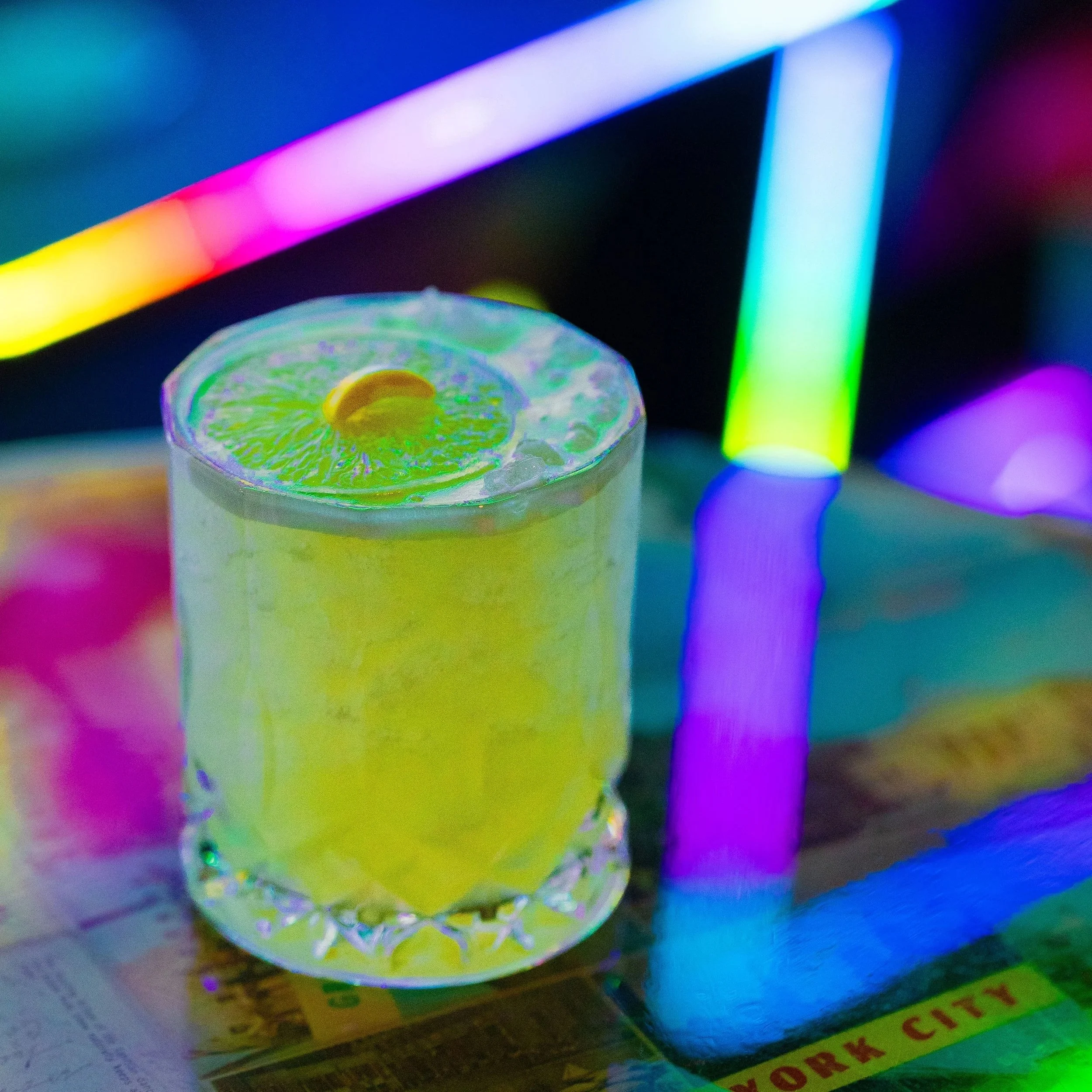 Bright Yellow Cocktail in a lowball glass lit up in front of neon