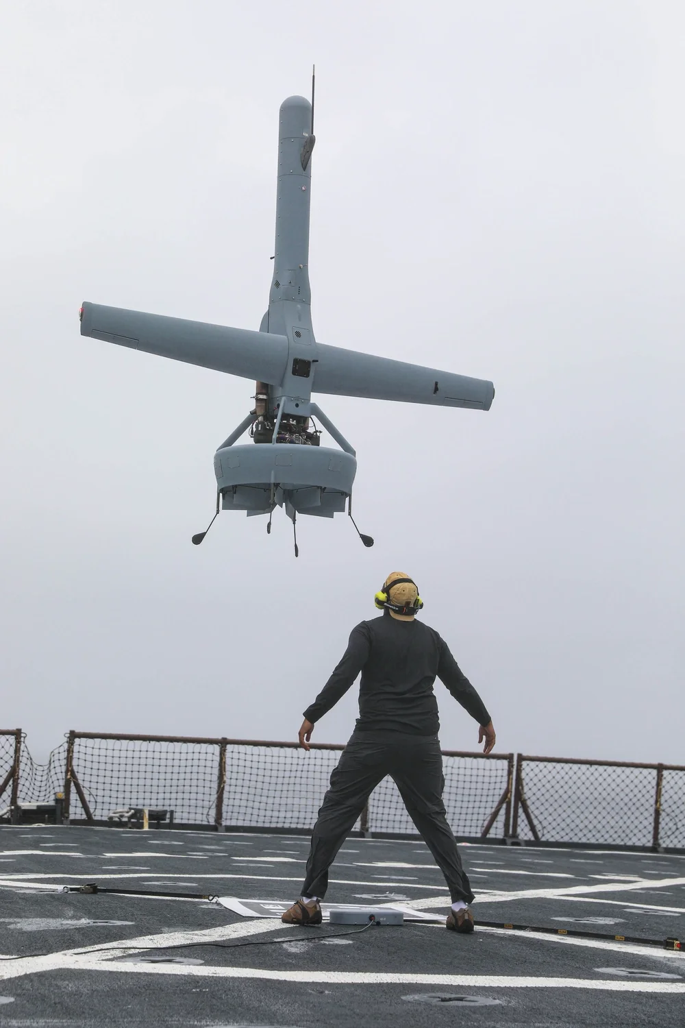 A V-BAT hovers above a civilian contractor on USS Carter Hall’s flight deck during a recovery test.