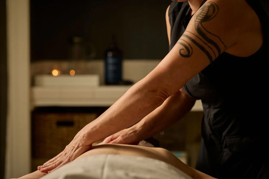 A massage therapist performing a massage on a person lying face down, with candles and a bottle in the background.