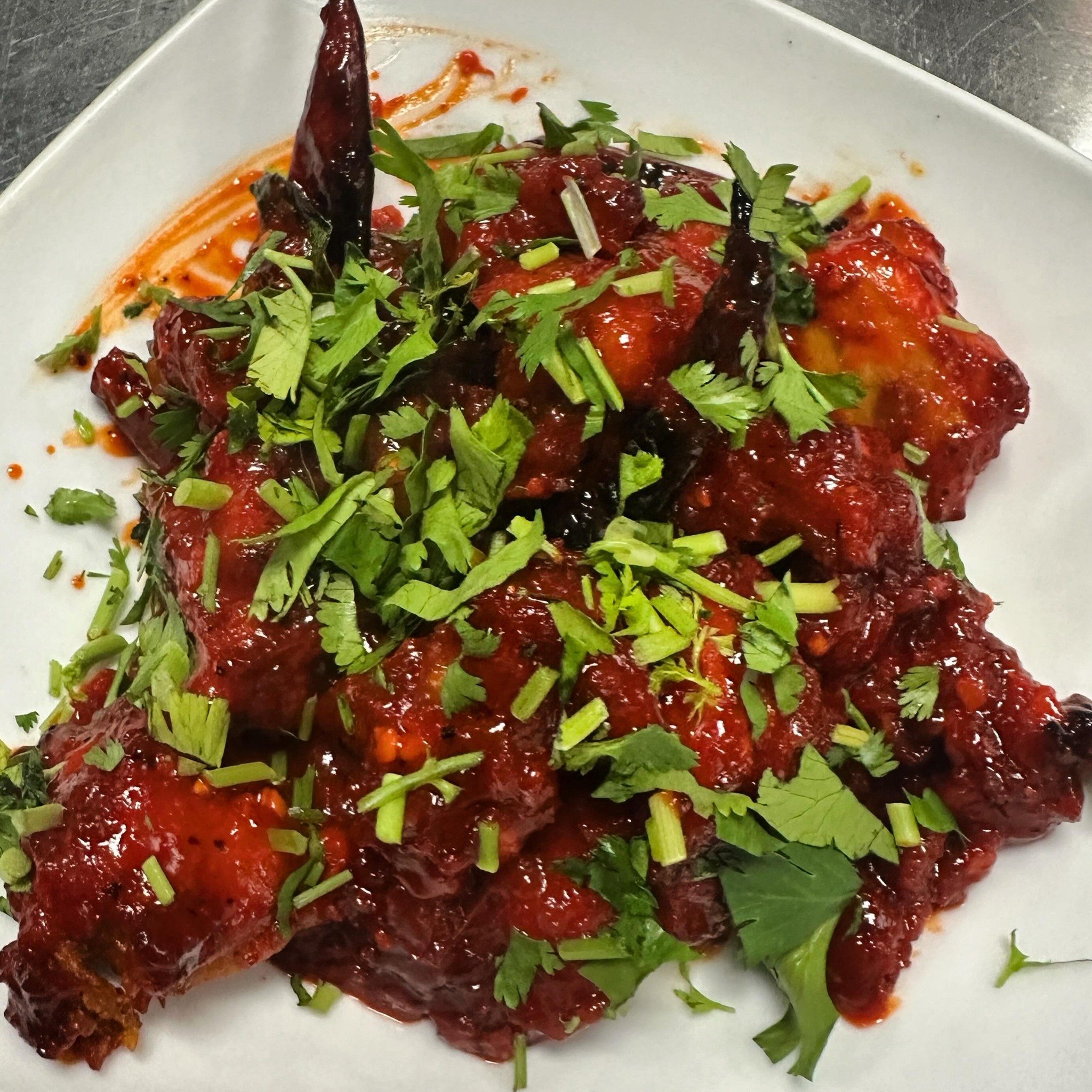 Pork ribs coated in barbecue sauce and garnished with chopped cilantro and sliced green onions served on a white plate.