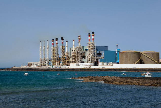 A large industrial power plant by the water with multiple smokestacks and cooling towers