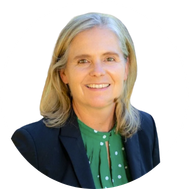 Michelle Rhodes- smiling woman with gray hair, wearing a dark blazer and a green blouse, in front of a white background.
