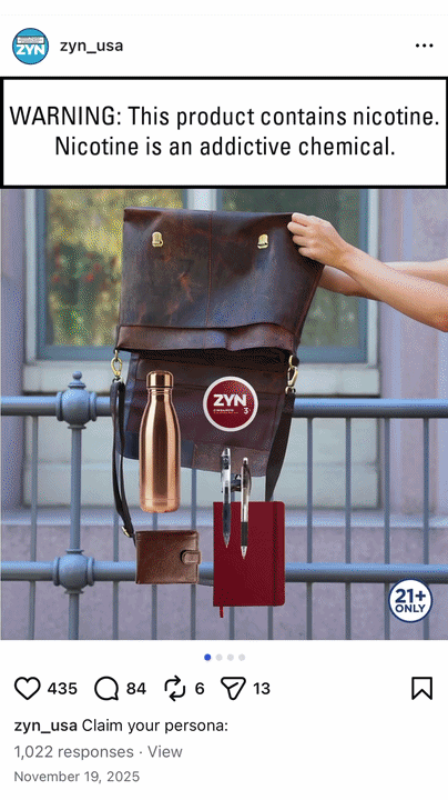 A leather bag hanging on a metal railing with a copper reusable water bottle and red and silver nicotine vaping devices attached to it, with a warning sign about nicotine in the background.