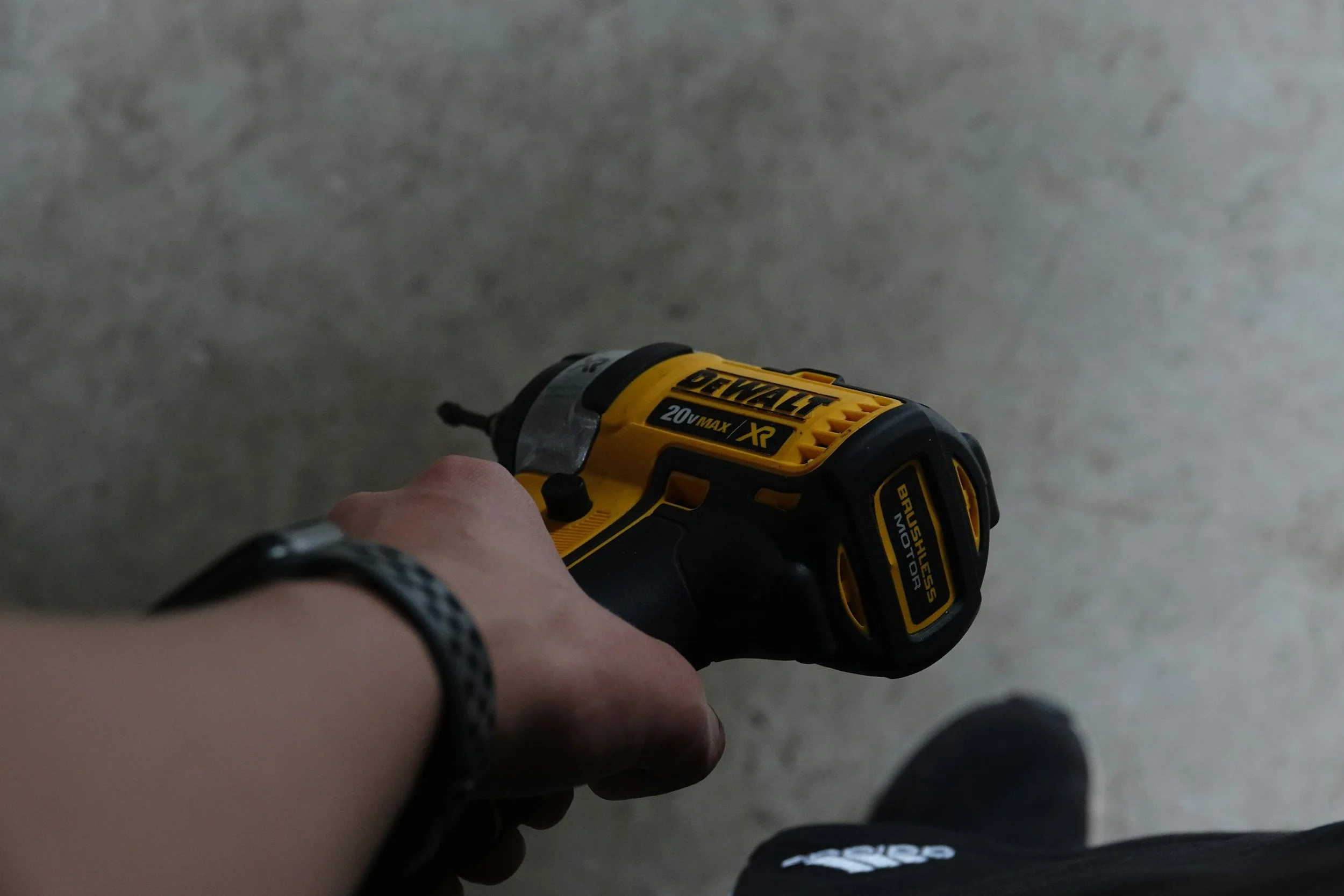 Hand holding a yellow Dewalt cordless power drill against a concrete wall background.