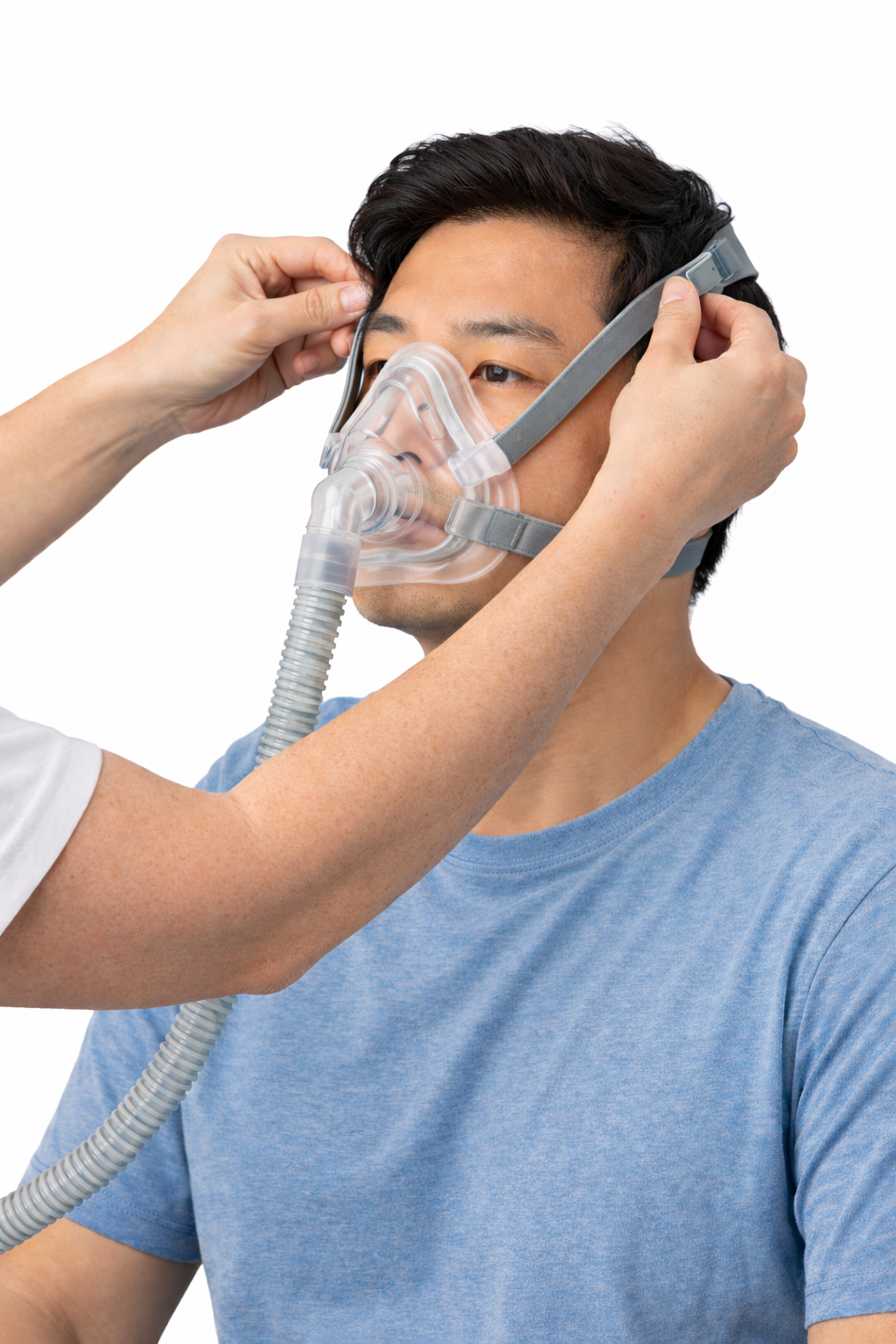 A man wearing a blue T-shirt puts on a non invasive breathing mask with assistance from another person.