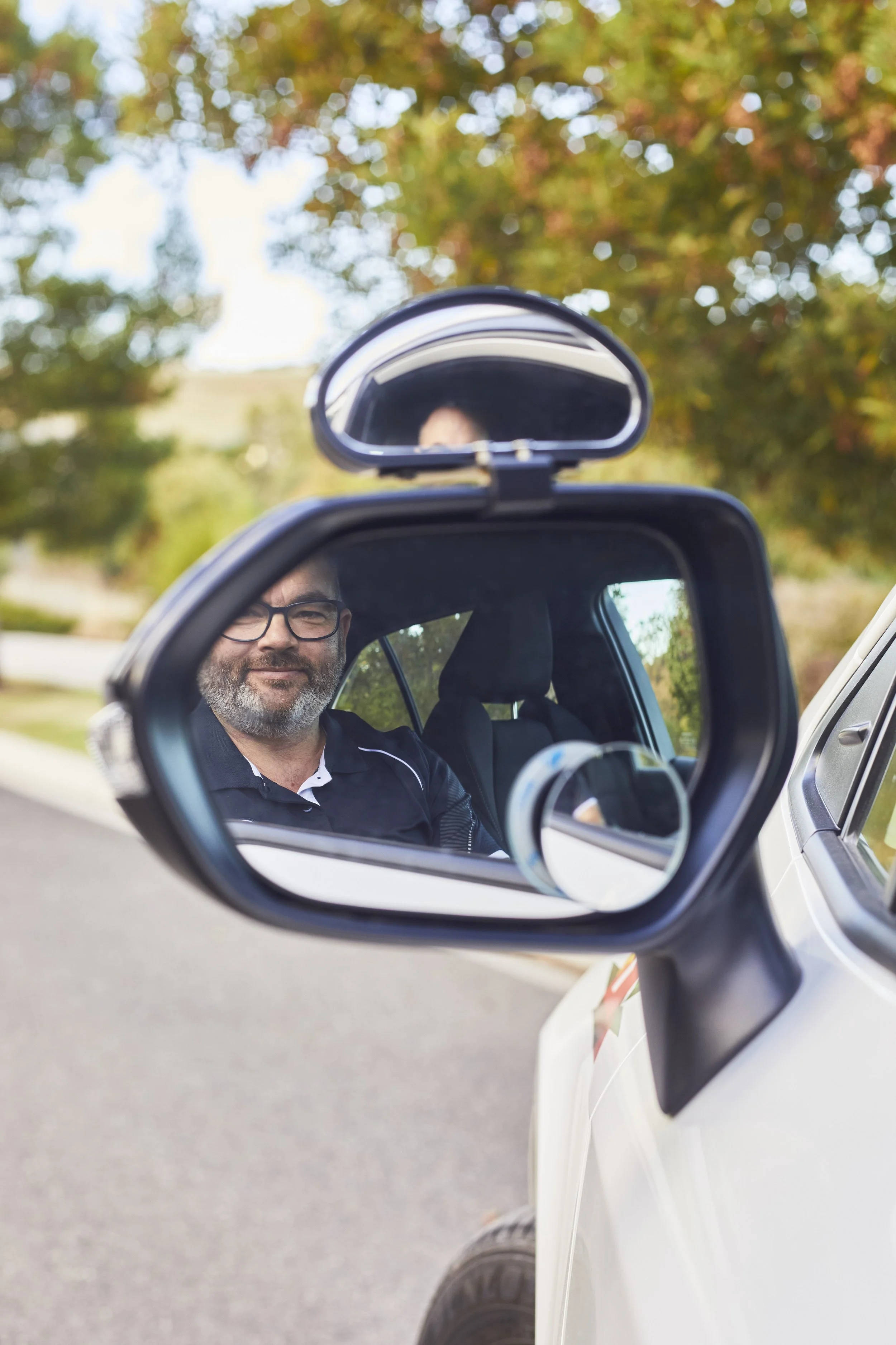 Ben D'Ornay, owner and driving instructor with RoadSafe Driver Training reflected in the side mirror of his car
