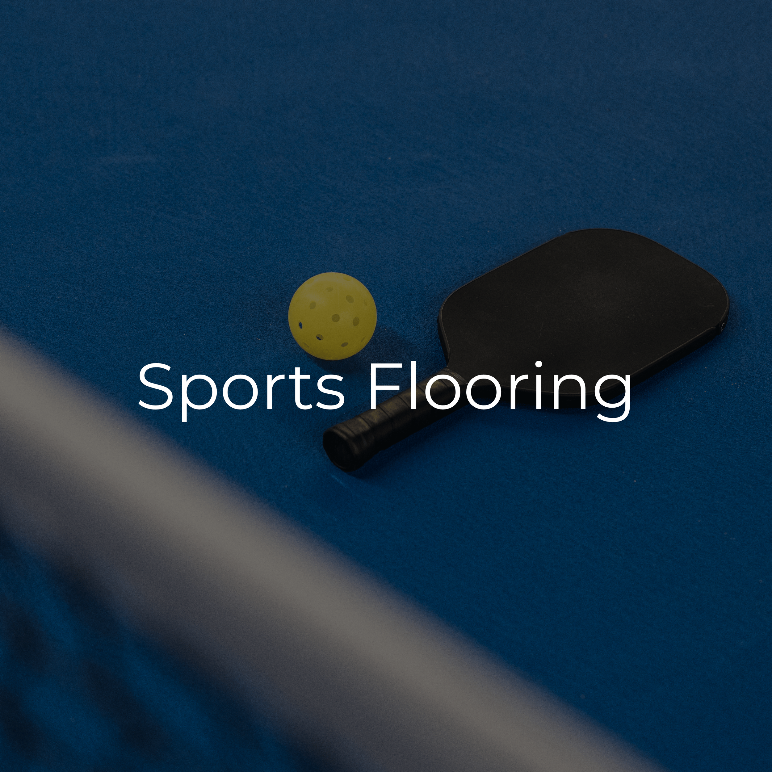 A yellow perforated ball and a black paddle lying on a blue sports flooring surface.