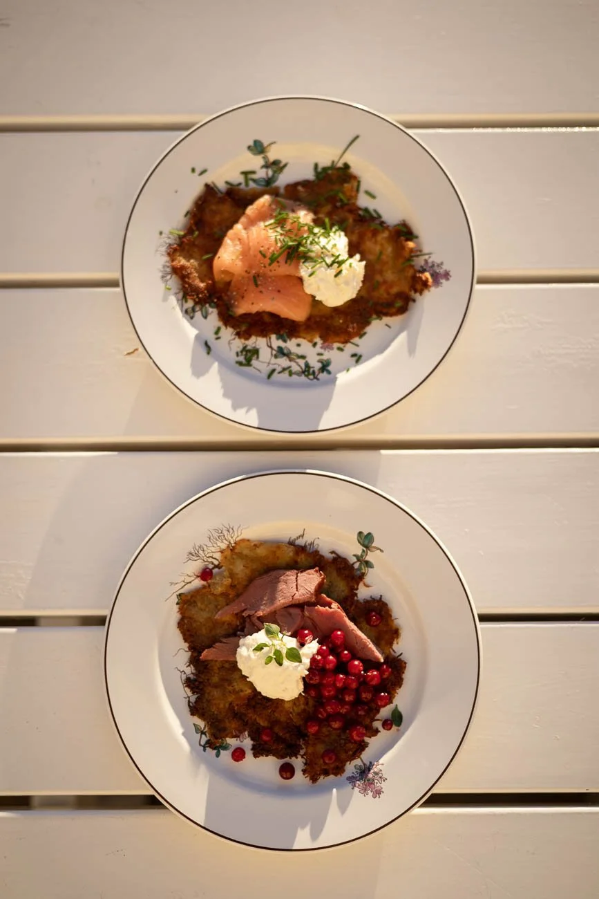 Två tallrikar med frysta, belagda med rå, röda vinbär, en bit skuret kött, gräslök, grädde och pommes frites, serverade på ett vitt träbord.