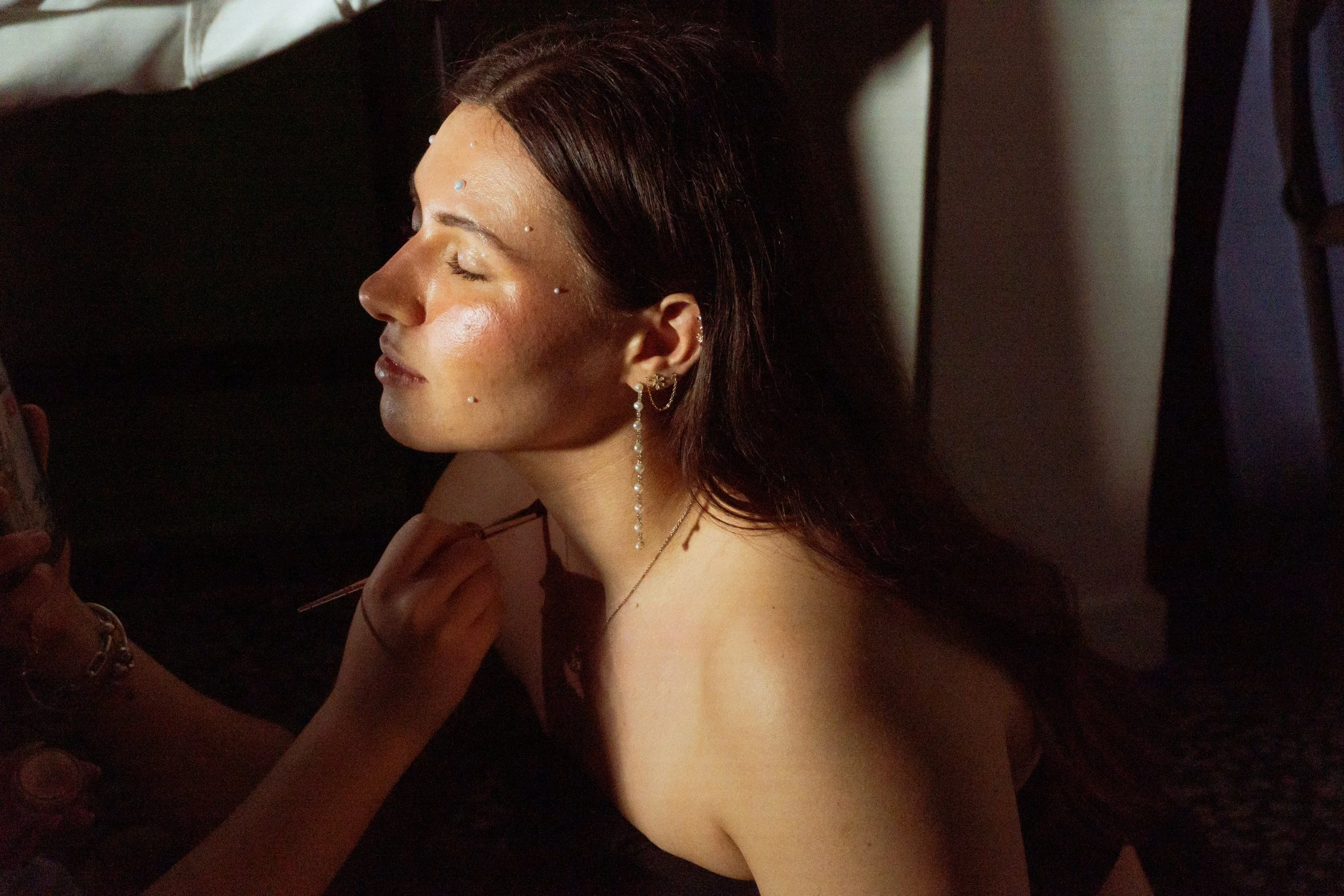 Femme avec des bijoux et des piercings, se faisant maquiller, dans une pièce sombre.