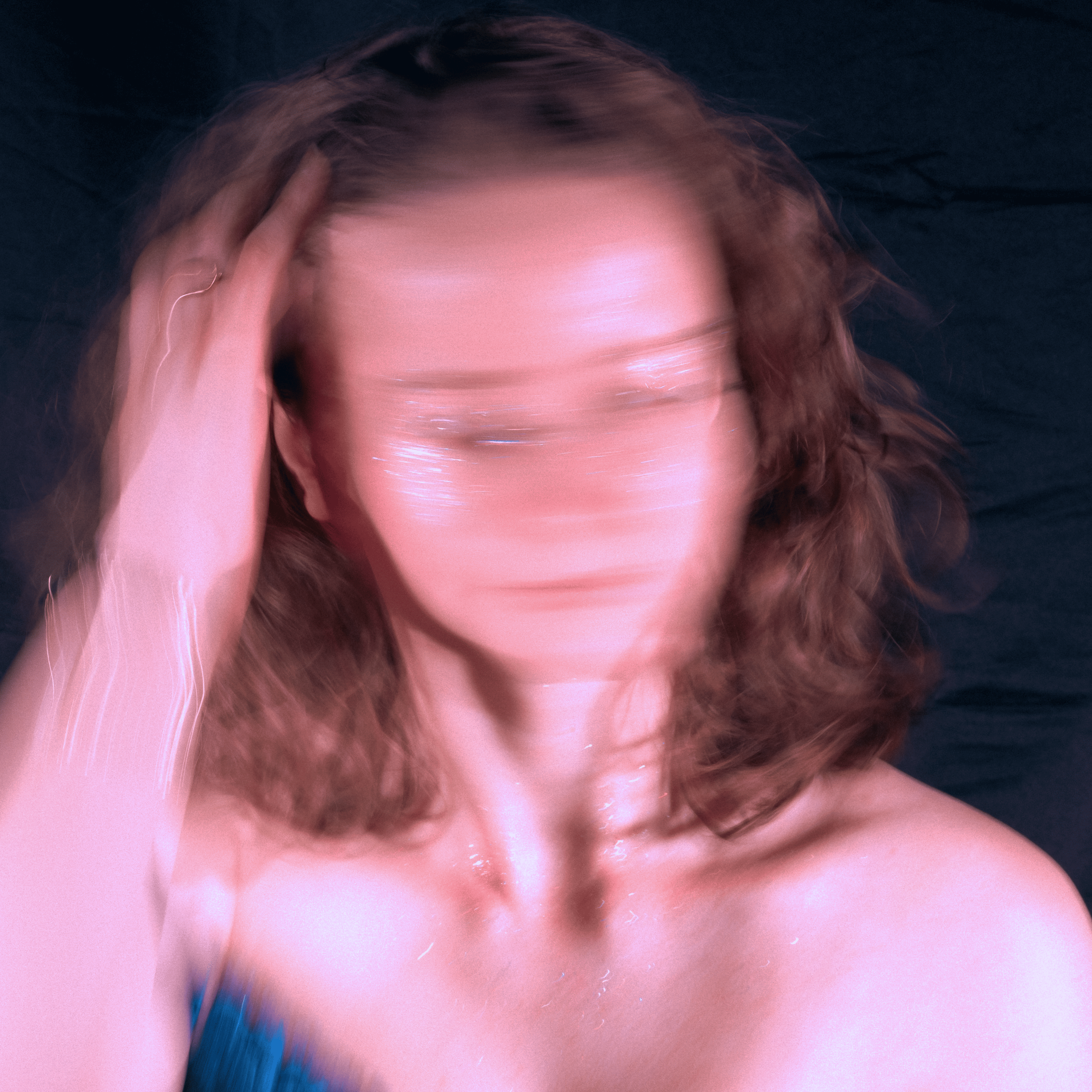 Photo floue d'une femme avec des cheveux bruns, sans visage identifiable, tenant sa tête avec une main, contre un fond sombre.