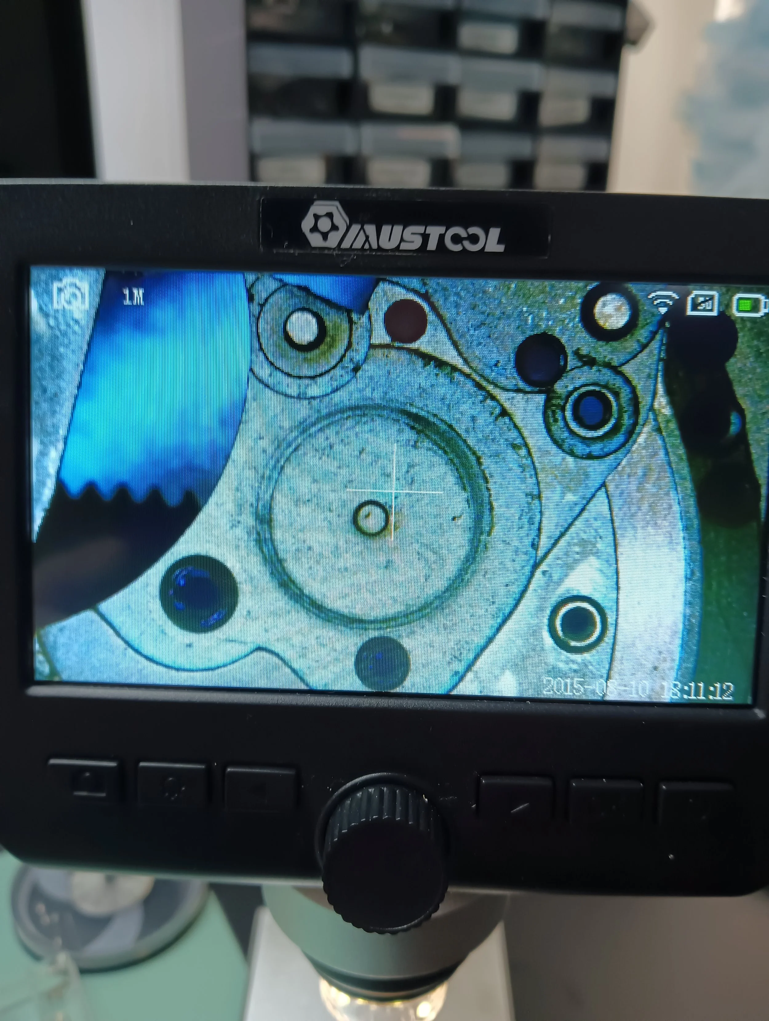 Close-up of a microscope displaying a detailed image of a mechanical gear system, with the brand name 'AUSTCOL' visible on the microscope's frame.