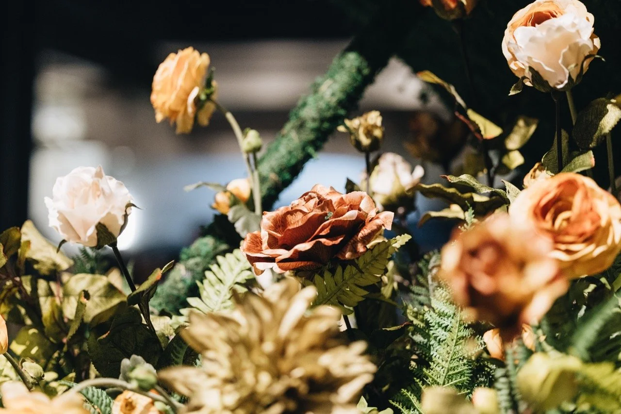 Artificial flowers with orange, white, and cream colors in a floral arrangement with green foliage.