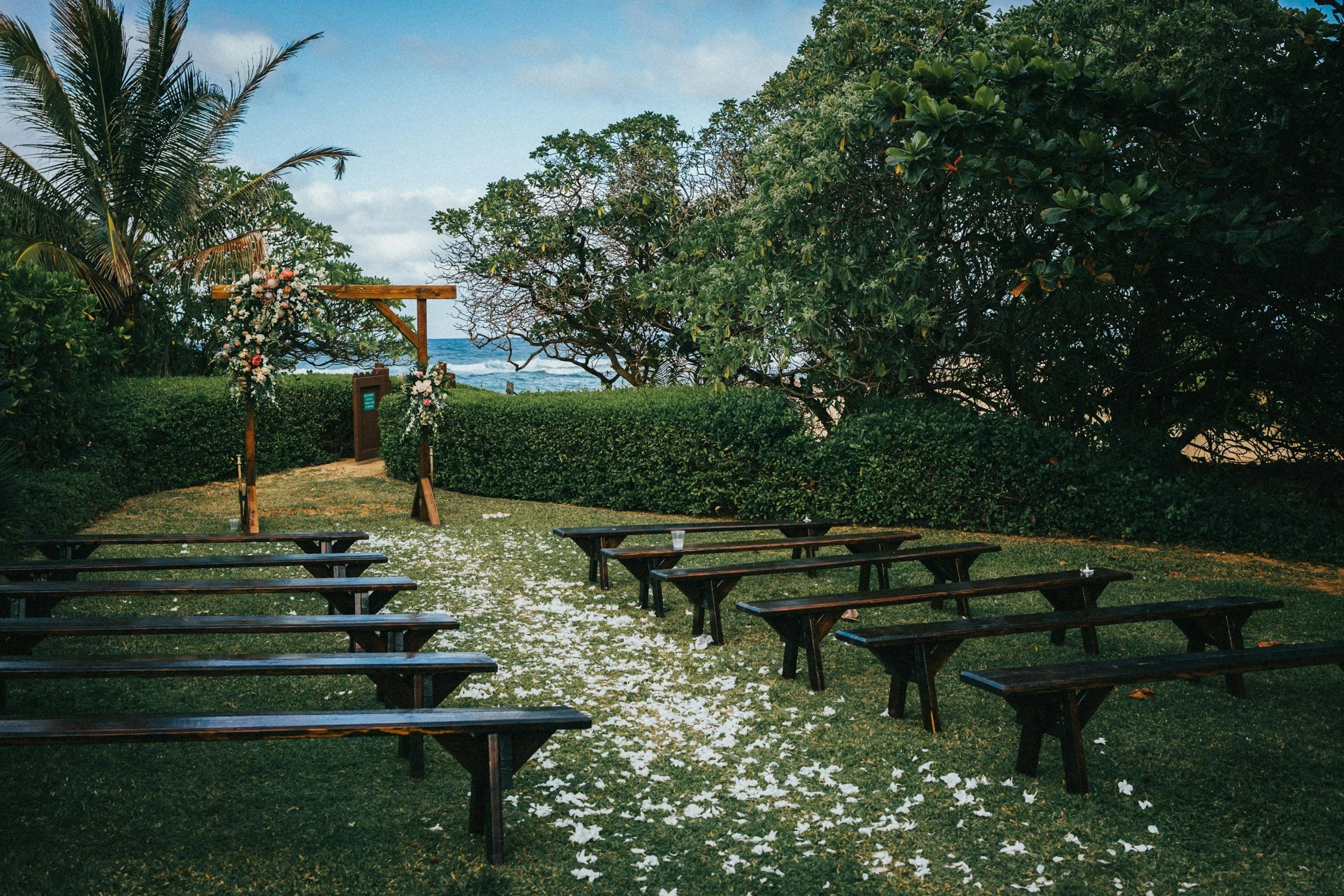 Outdoor wedding ceremony setup with benches, floral arch, and ocean view in the background.