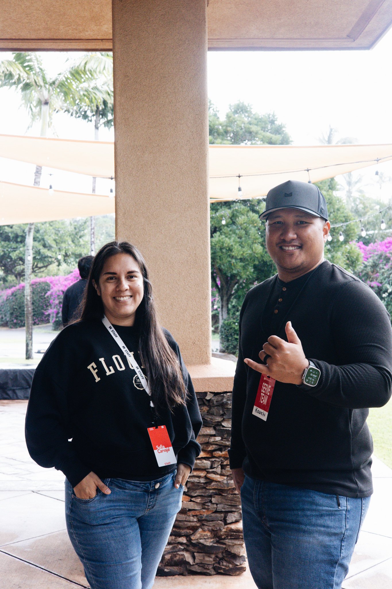 A family of three, a woman, a man, and a young boy, smiling and posing together indoors, with a colorful abstract mural in the background.