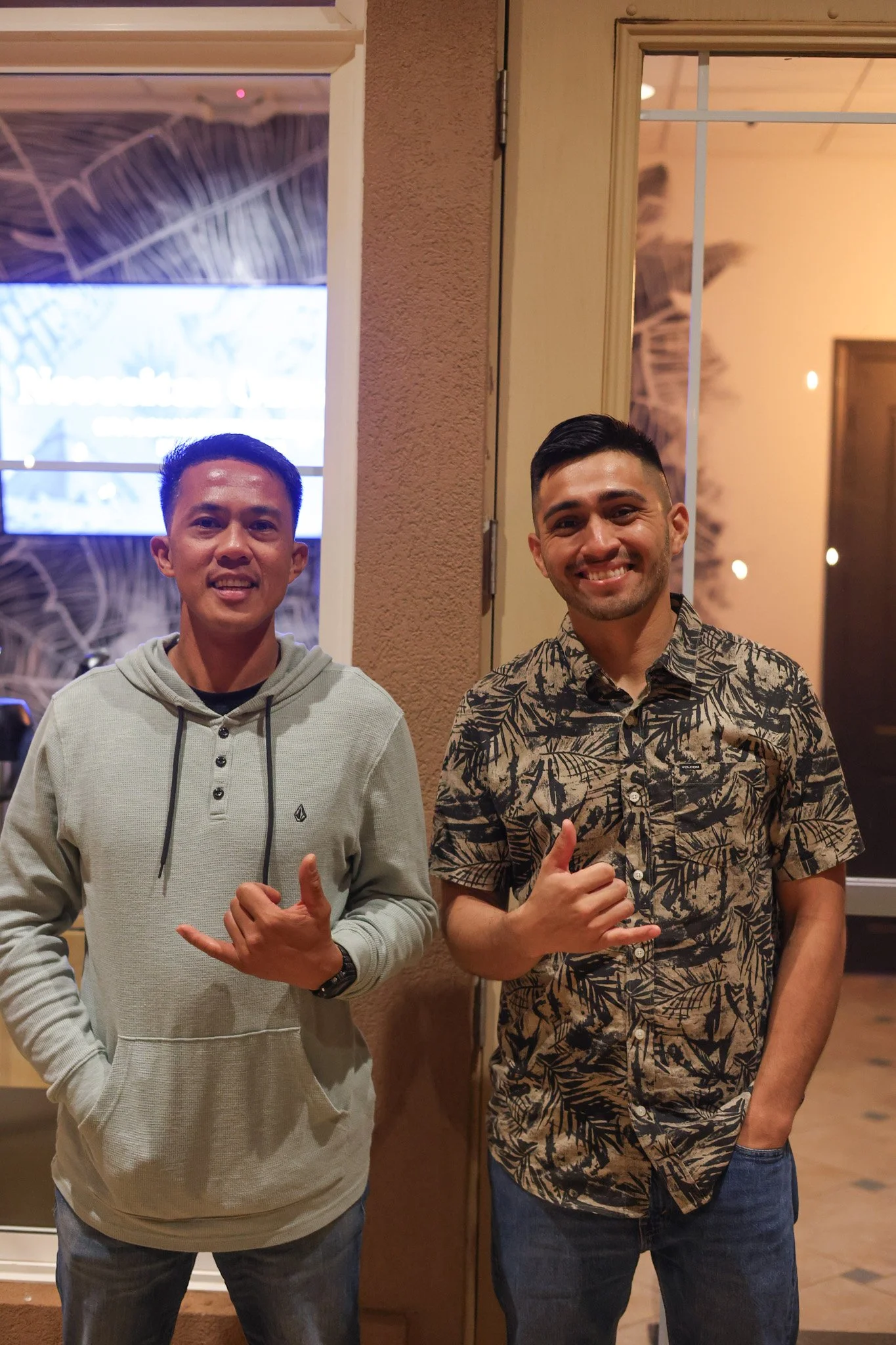 Group of six young adults smiling at the camera indoors, holding cups and snacks, with a mural of a person's face on the wall behind them.