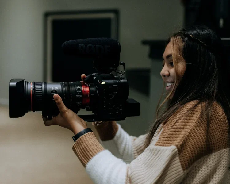 Woman operating a professional video camera with a microphone attached indoors.