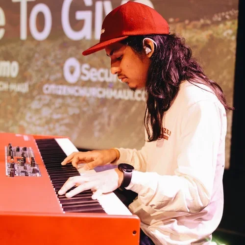 Person wearing a red cap, playing a red keyboard at an event.