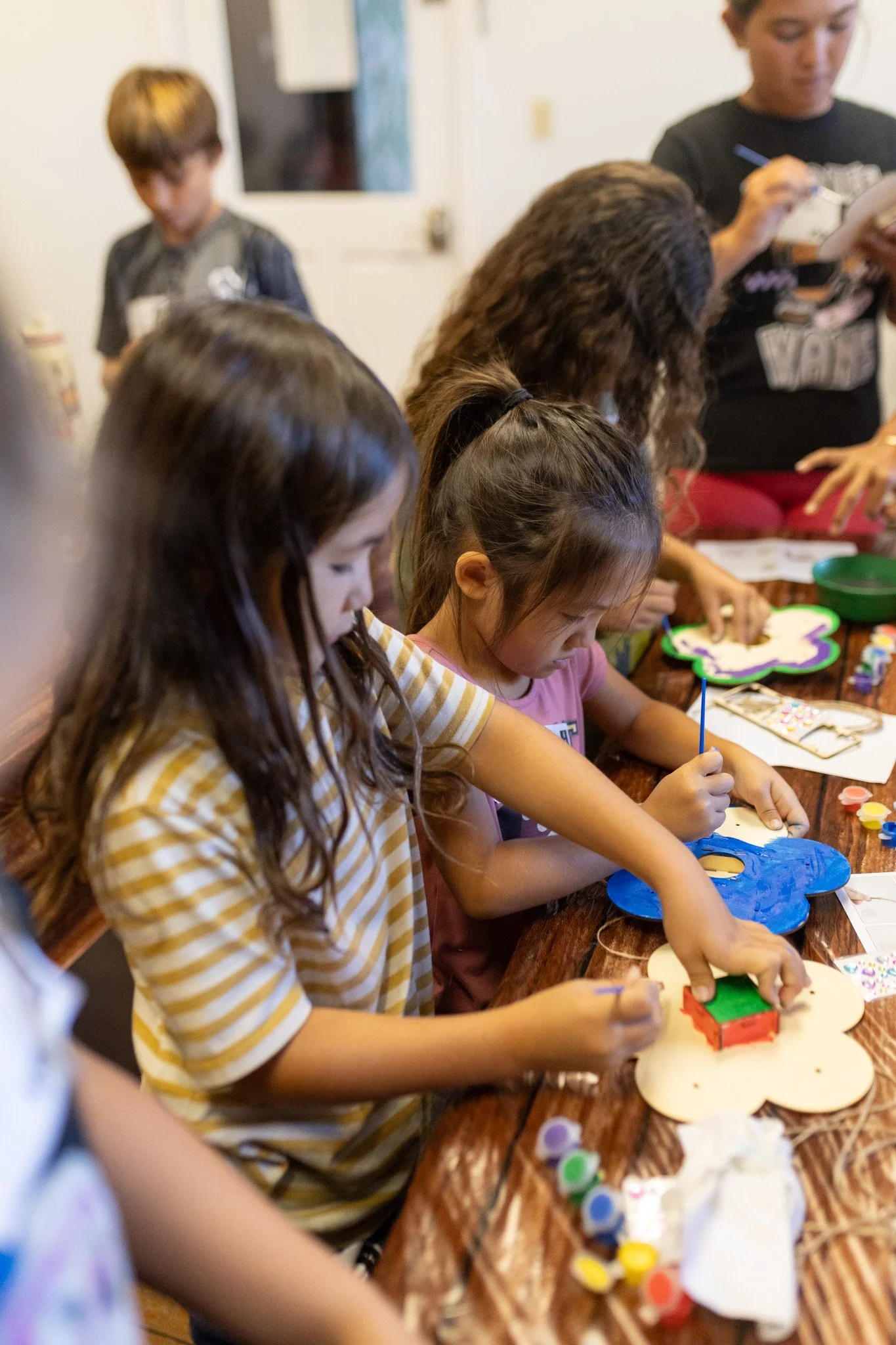 Children decorating cookies at a table, with an adult in the background.
