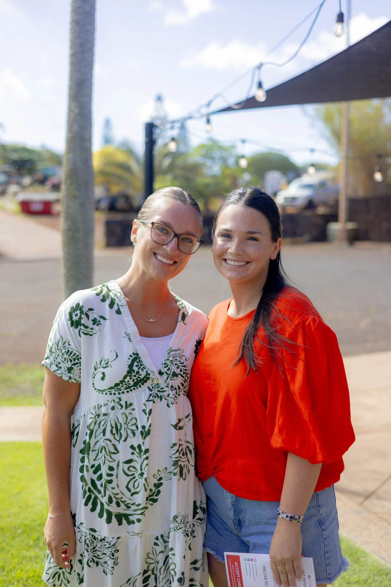 Two women smiling and holding coffee cups, standing near a large window in a modern office space.