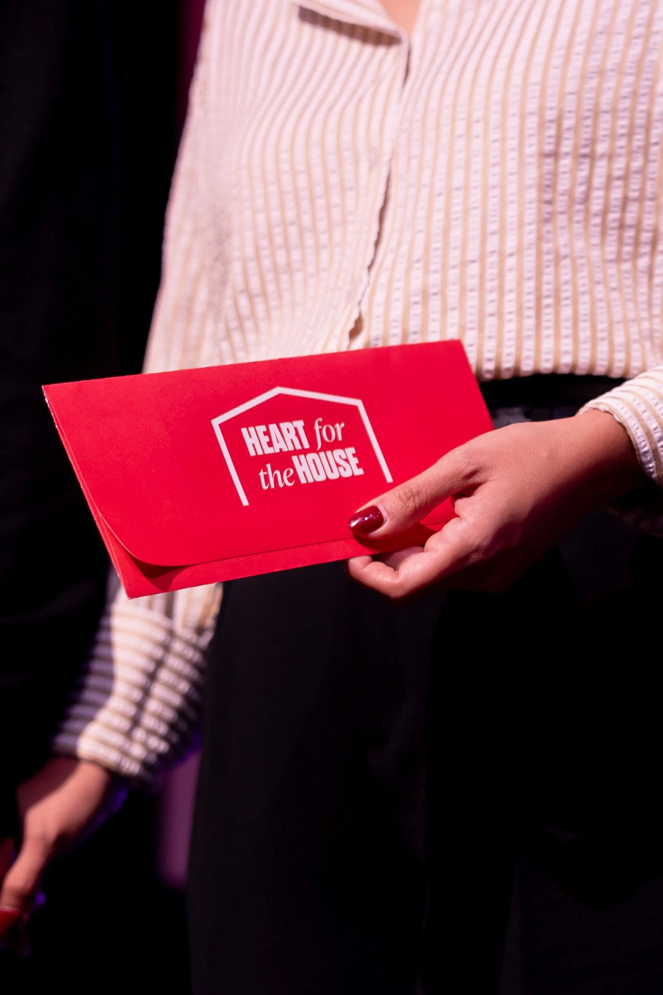 A person holding a red envelope with the text 'HEART for the HOUSE' printed on it.