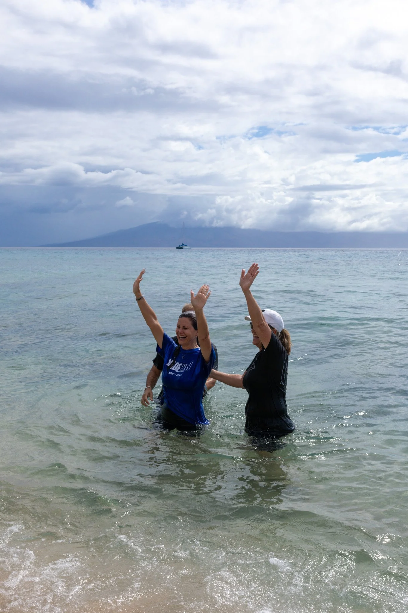 A family of three, a woman, a man, and a young boy, smiling and posing together indoors, with a colorful abstract mural in the background.