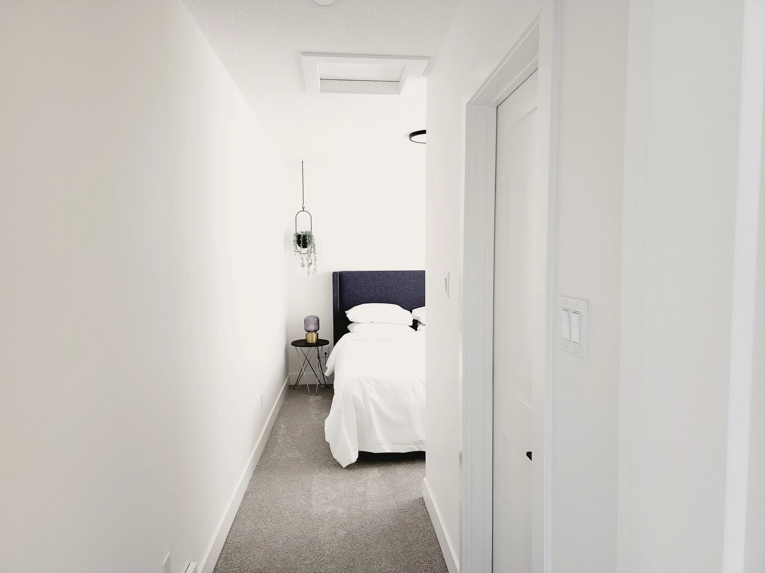 neutrally styled bedroom with gold lamp on side table and hanging plant