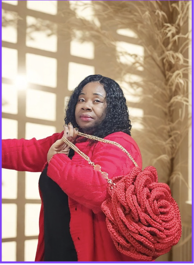 A woman with curly black hair wearing a red coat and holding a large red knitted bag over her shoulder.