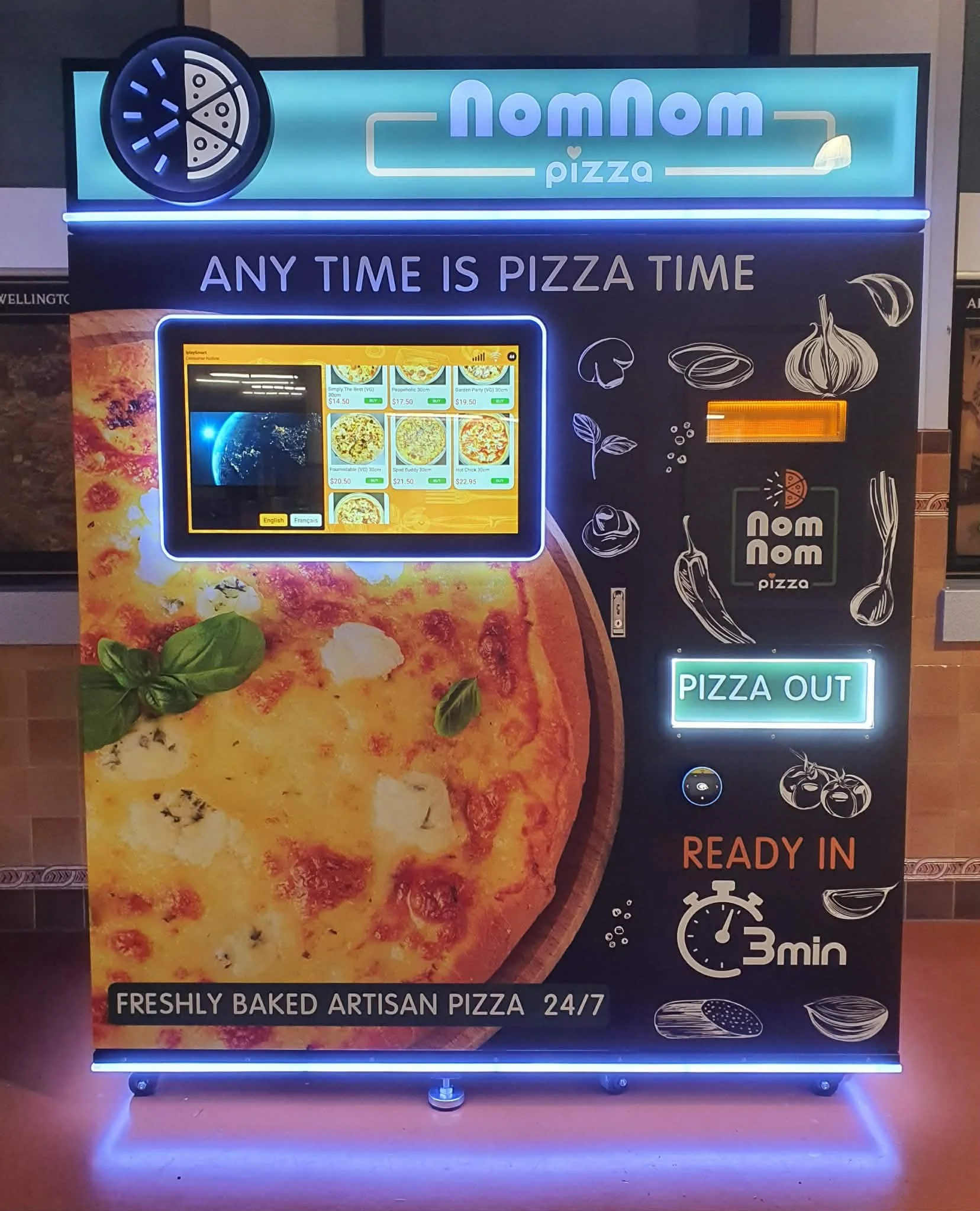 NomNom Pizza vending machine featuring a large image of a pizza with basil, a digital menu screen, and text indicating 24/7 artisan pizza with a 3-minute wait for ready pizzas.