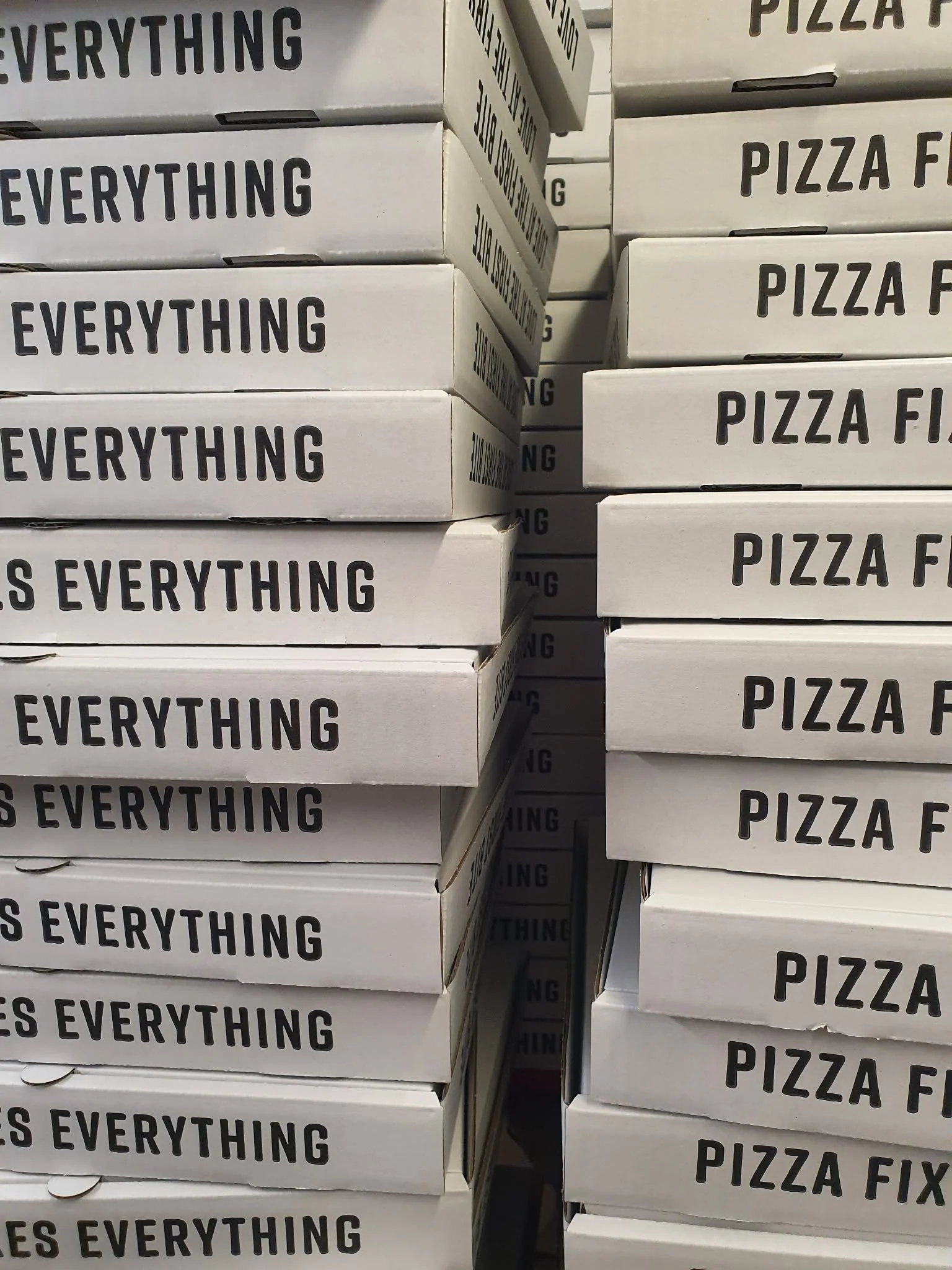Stacked pizza boxes with labels 'PIZZA FIXES EVERYTHING' on a shelf.