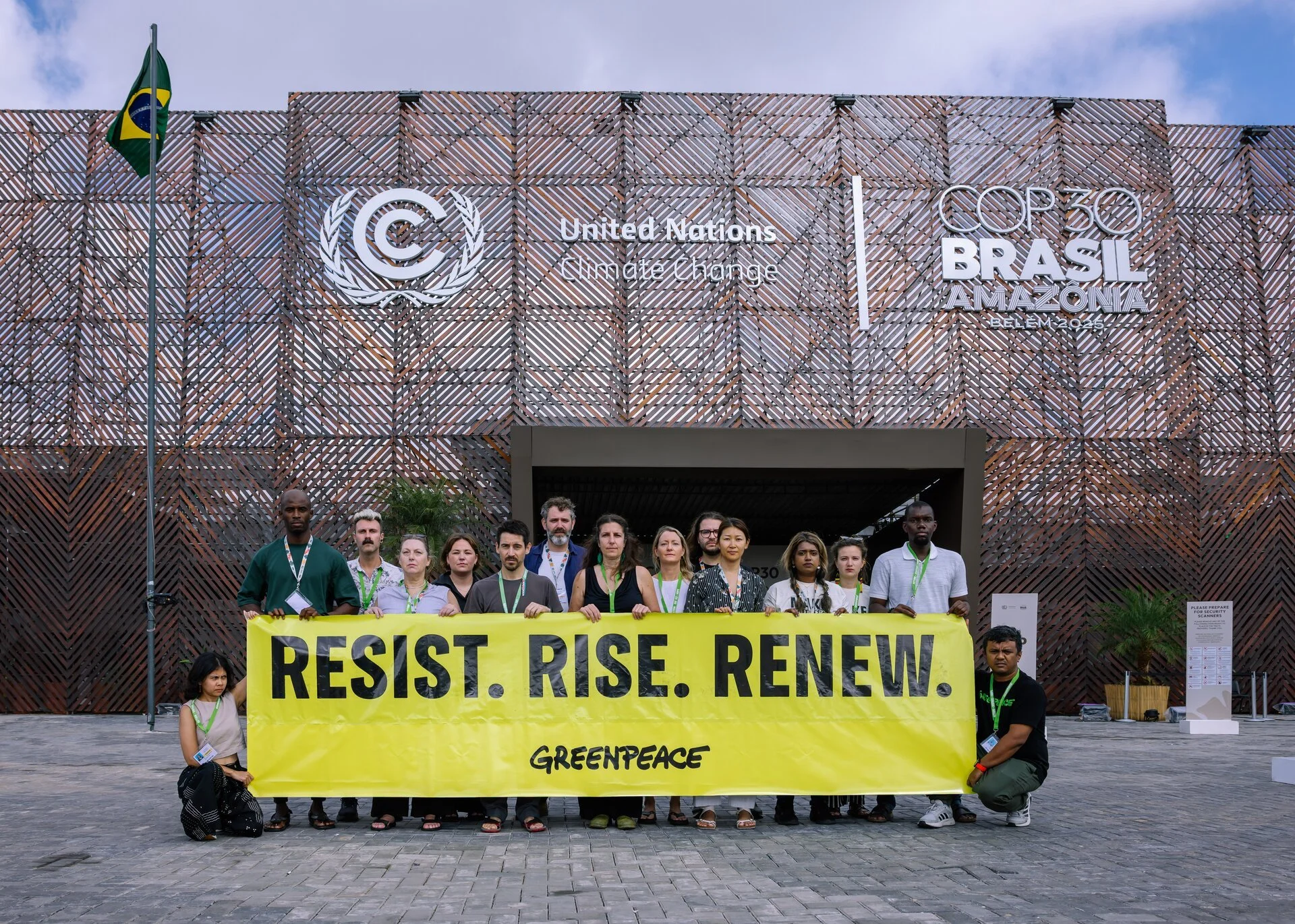 Gruppe von Menschen bei einem Protest vor einem Gebäude mit dem Logo der UN-Klimakonferenz COP30. Sie halten ein großes gelbes Banner mit der Aufschrift "Resist. Rise. Renew." von Greenpeace. Es sind überwiegend junge Erwachsene, einige tragen grüne Lanyards.