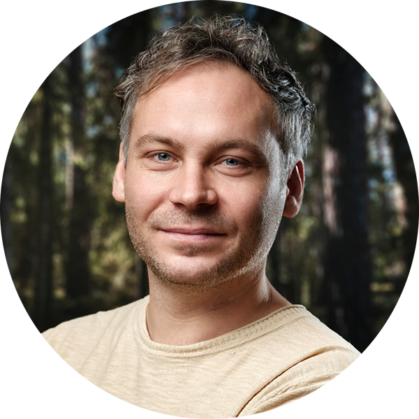Junger Mann mit Kurzhaarschnitt und dezentem Lächeln, stehender Hintergrund mit Bäumen in einem Wald.