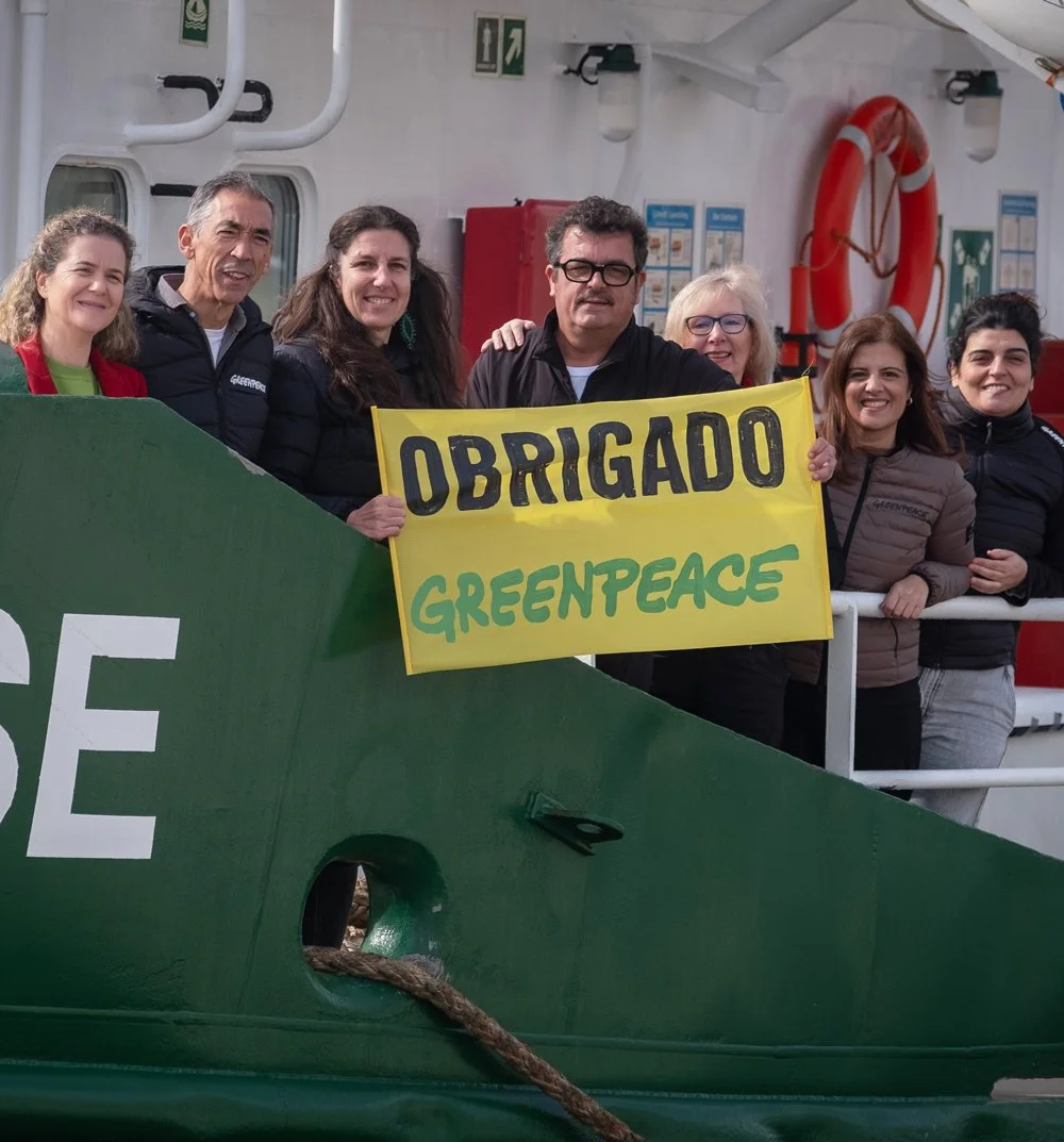 Gruppen von Greenpeace-Aktivisten auf einem Schiff, die eine gelbe Schilder mit der Aufschrift 'OBRIGADO GREENPEACE' halten.