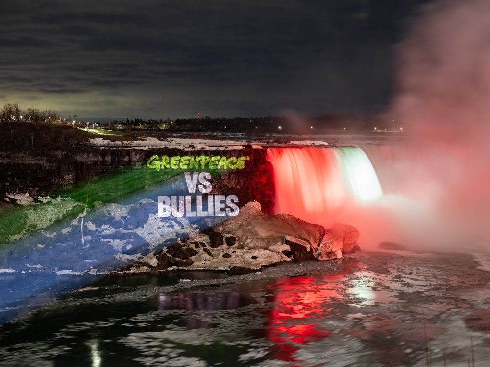 Der Niagarafall bei Nacht, beleuchtet in den Farben der italienischen Flagge, mit der Aufschrift "Greenpeace vs Bullies" im Wasser.