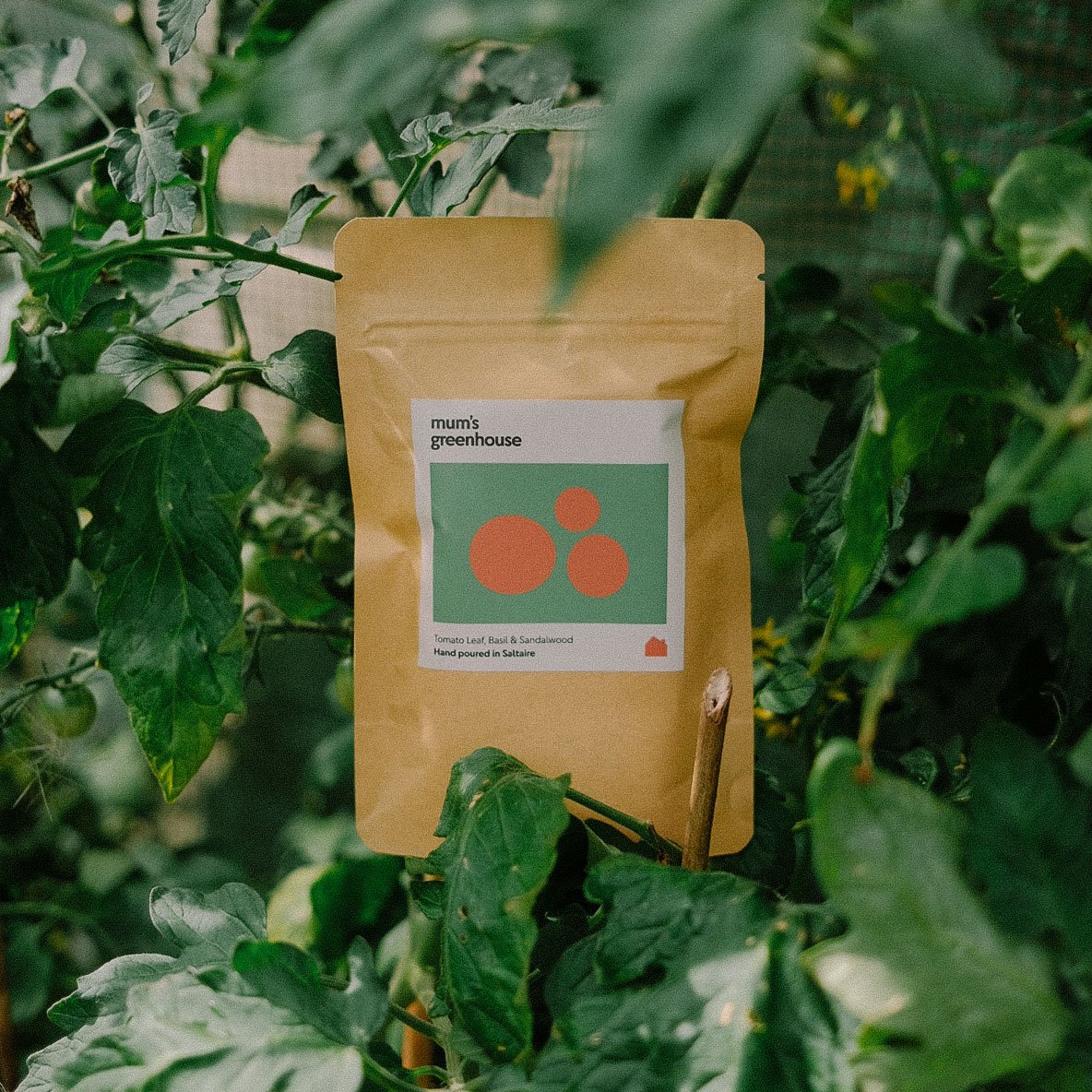 A packet of Mum's Greenhouse plant food among green leaves and plants.