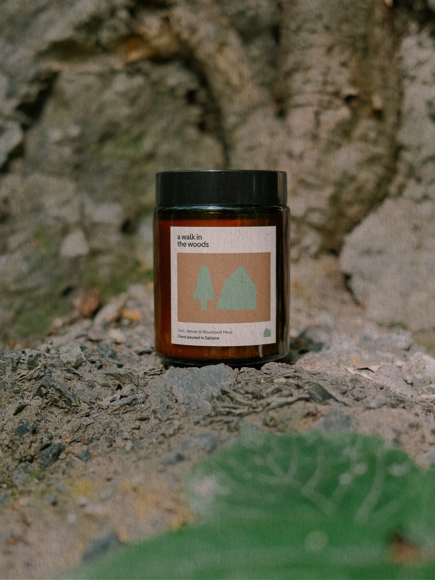 A brown bottle with a black lid placed on the ground, with a blurred background of uneven rocks and patches of grass.