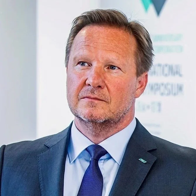 Ein Mann in formeller Kleidung, vor einem weißen Hintergrund mit Text. Geschäftsführer von GC Austria Ronald Dörflinger.