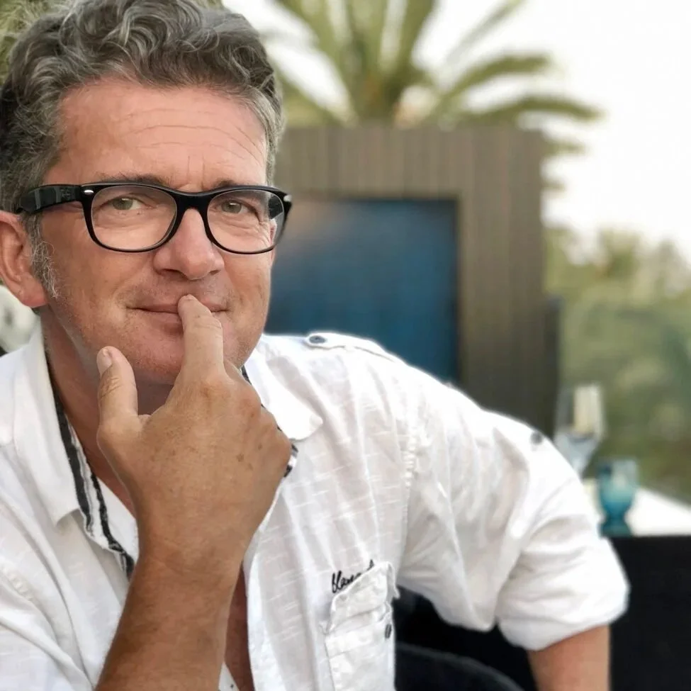 Ein Mann mit Brille und grauem Haar lächelt nachdenklich mit der Hand am Kinn. Alexander Doepel welcher Schreibseminare organisiert.